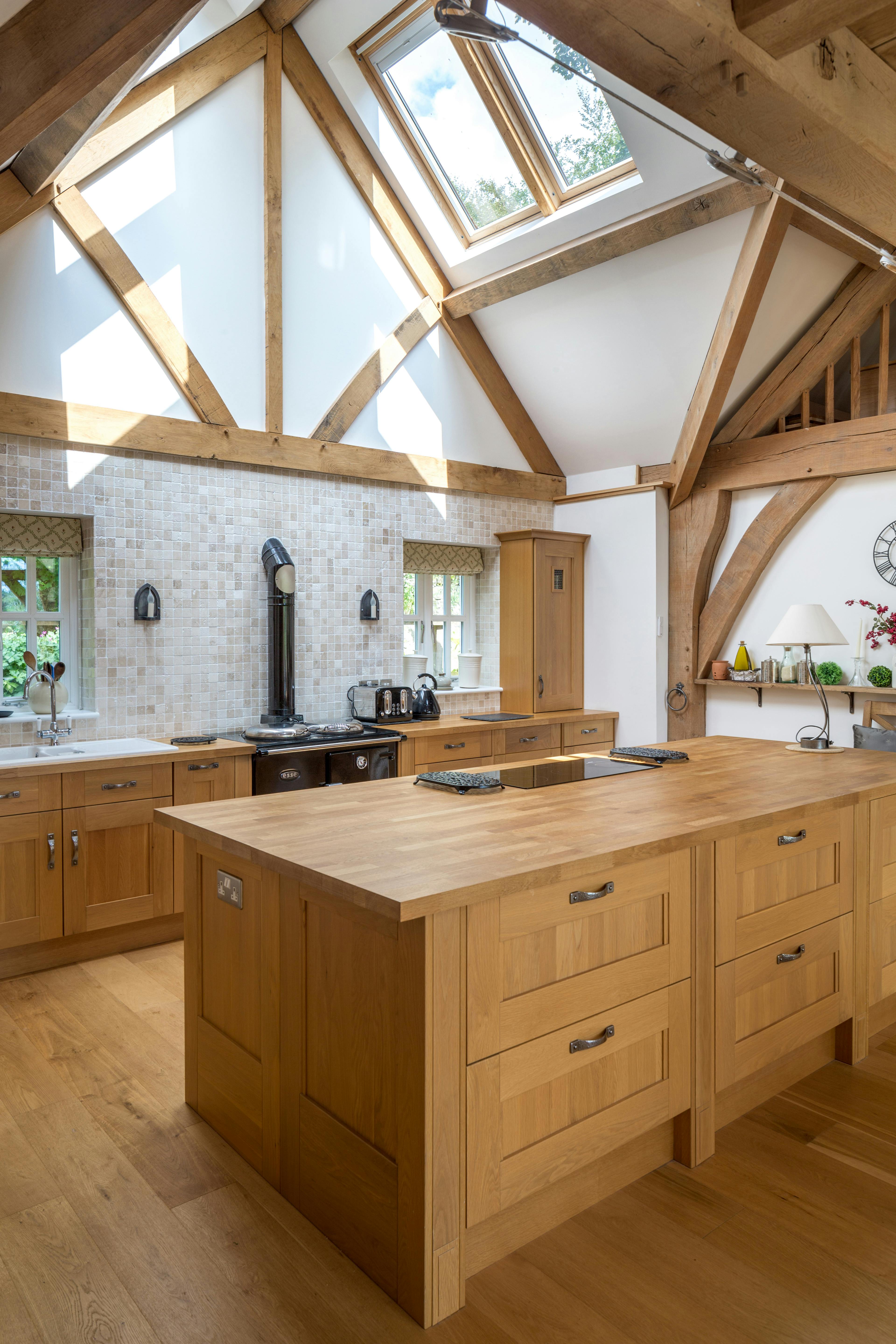 An oak framed kitchen with a wooden island and with sun coming through a rooflight
