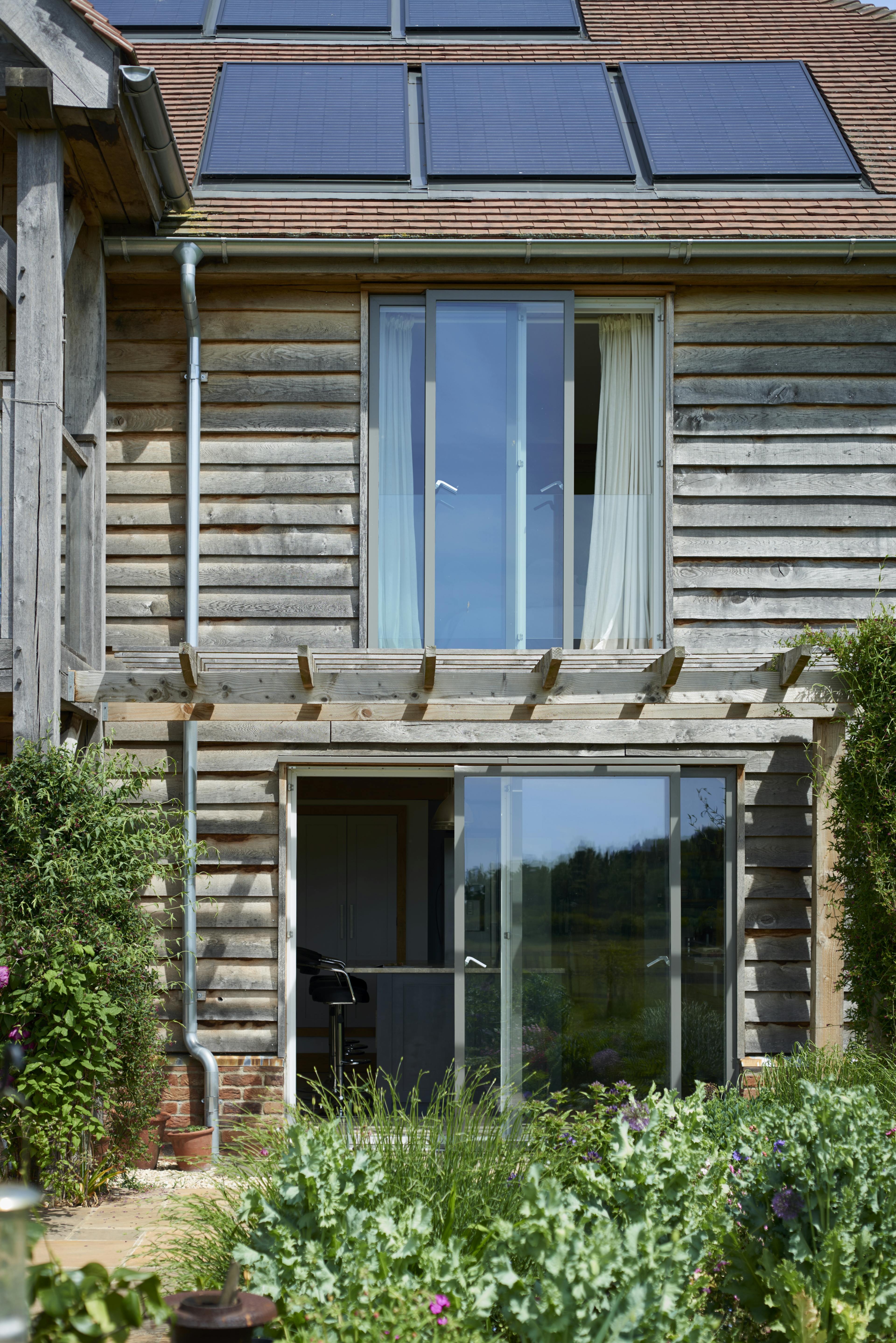 Timber clad large oak framed home with sliding doors, showing back garden and flowers