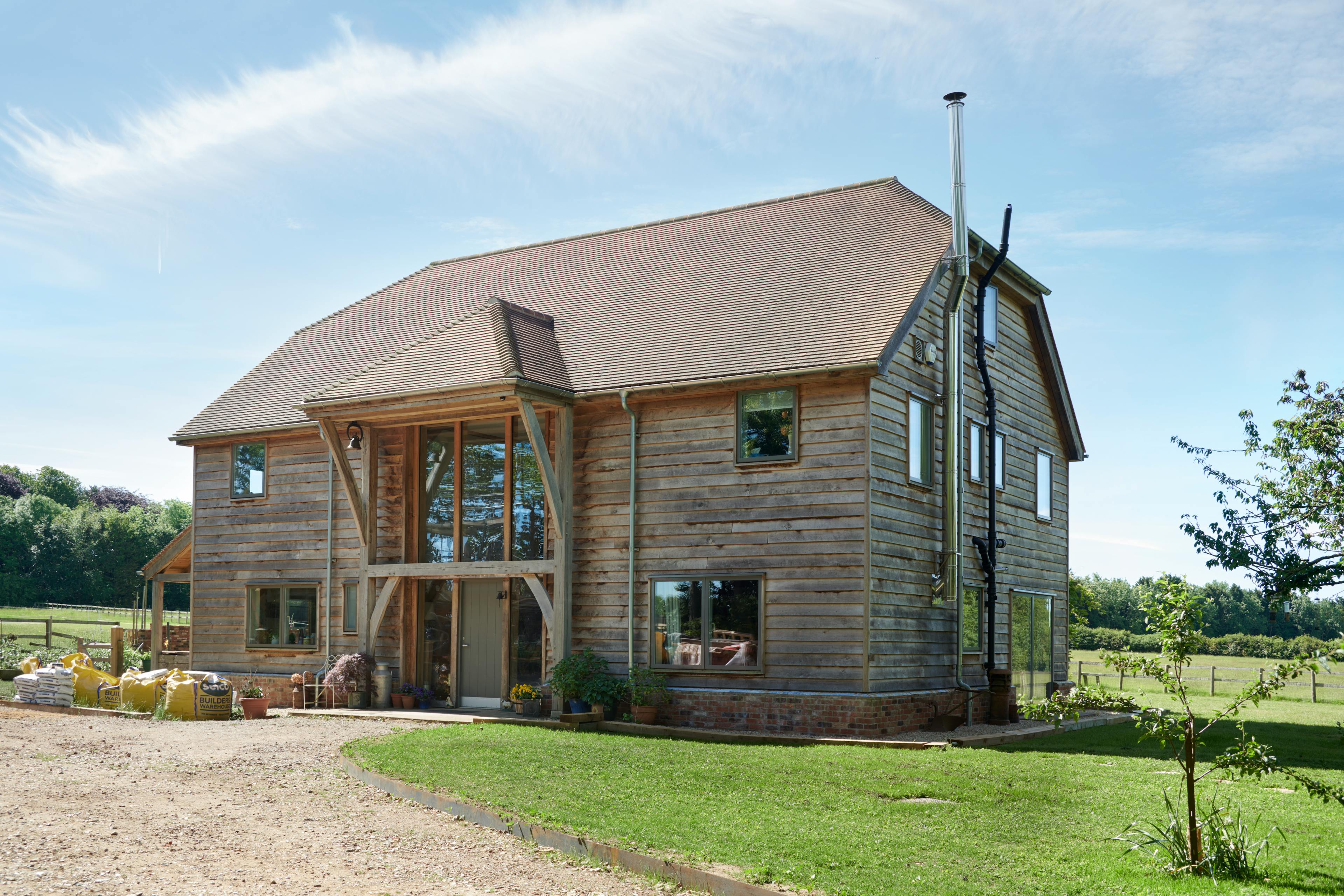 A timber clad oak framed 2 storey house with a garden and large green lawn on a sunny day with a blue sky