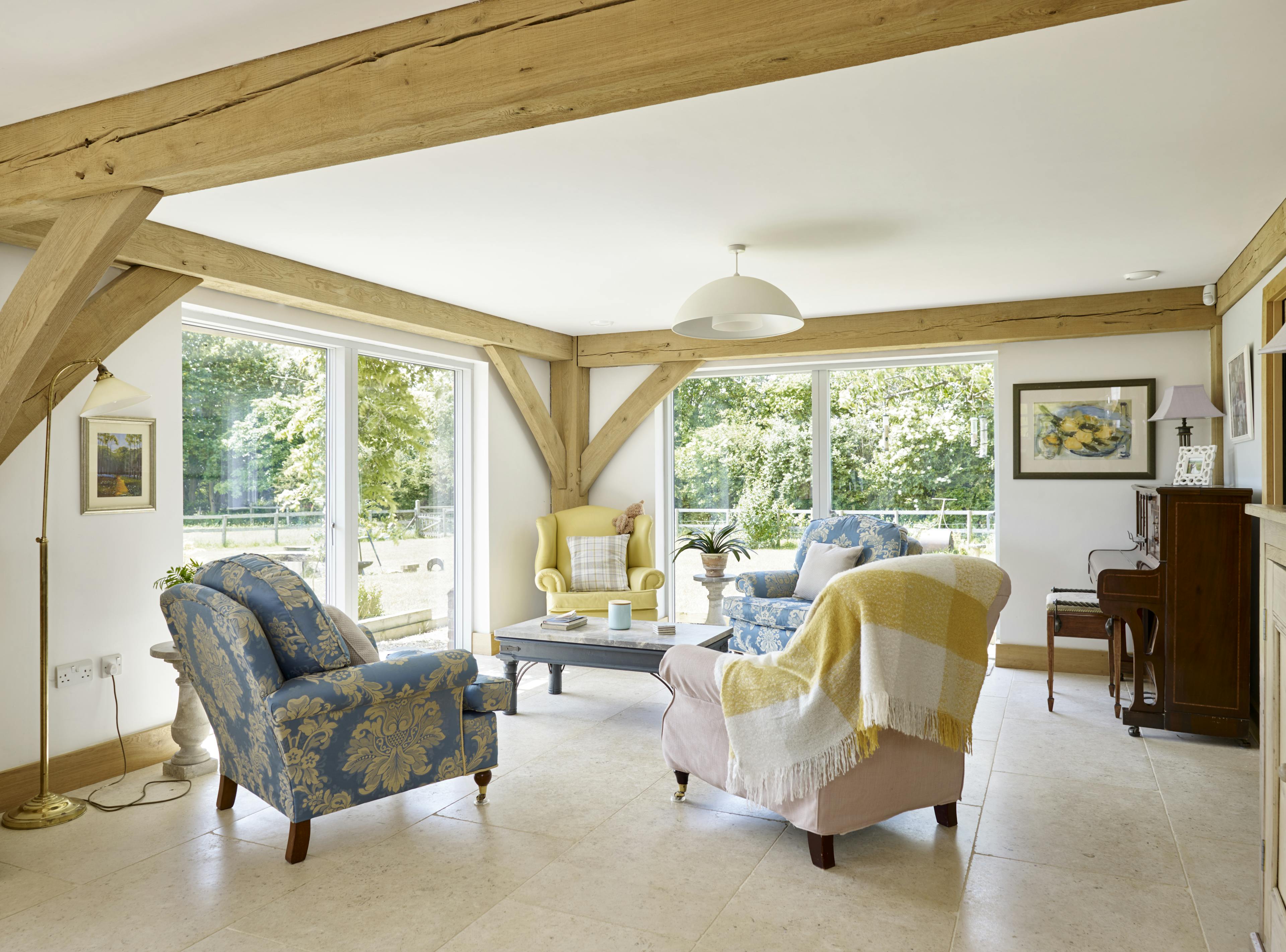 A light filled oak framed sitting area with armchairs and a piano