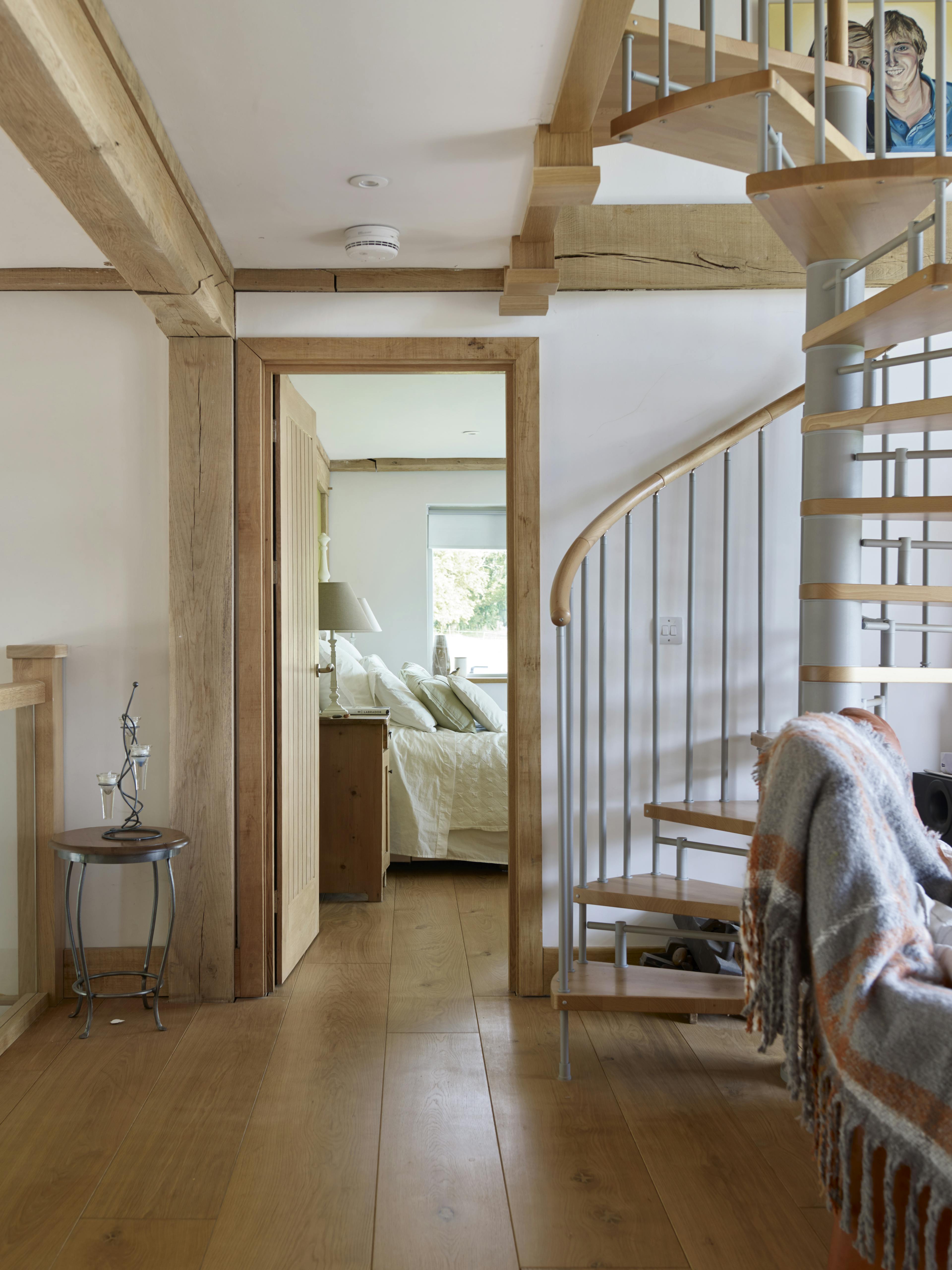 An oak framed home interior showing  spiral stairs and a door opening to a bedroom