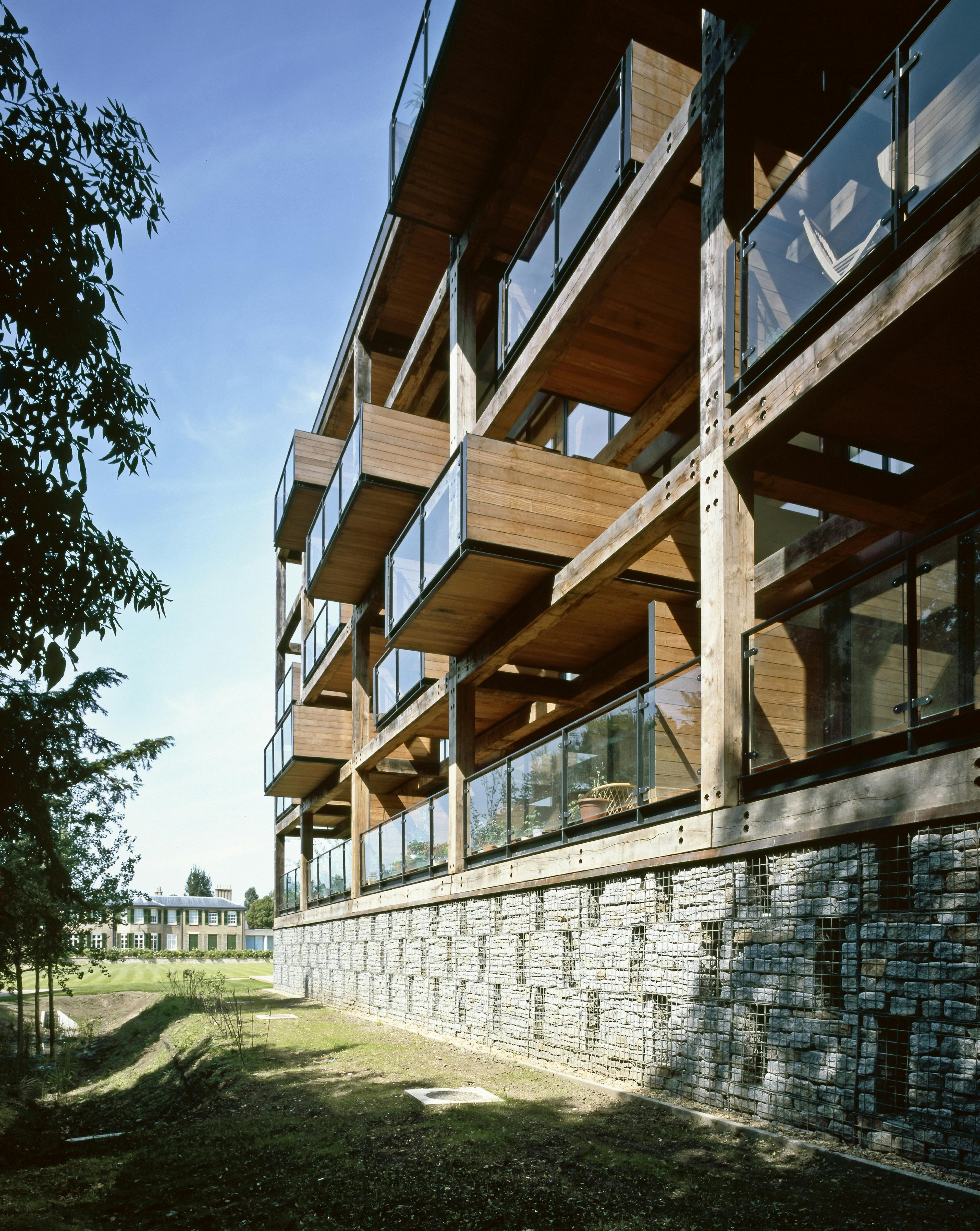 Exterior view of an apartment building showcasing oak-framed balconies secured with steel fixings, providing a striking contrast to the surrounding environment.