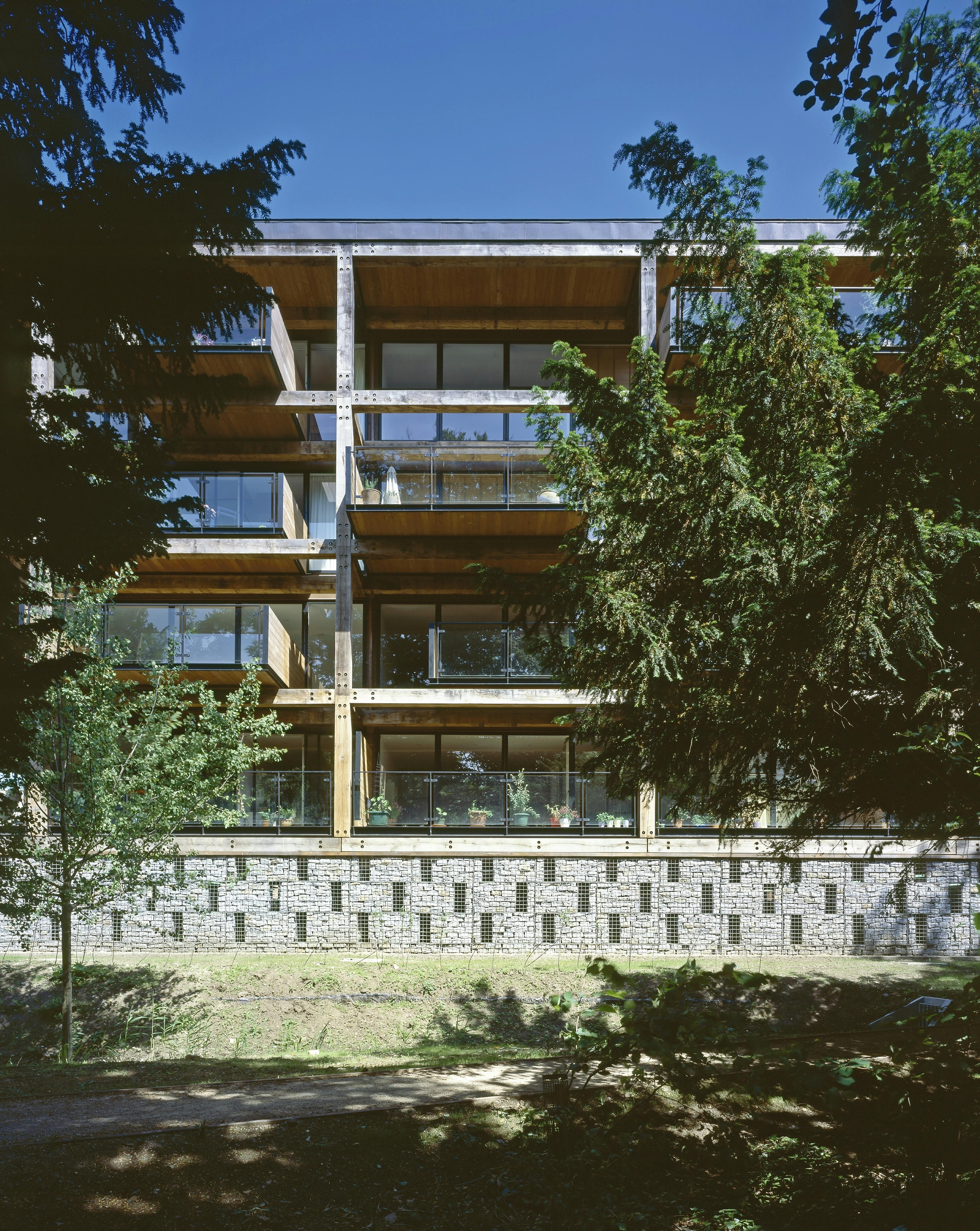 Exterior view of an apartment building featuring oak-framed balconies secured with steel fixings, situated amidst natural surroundings