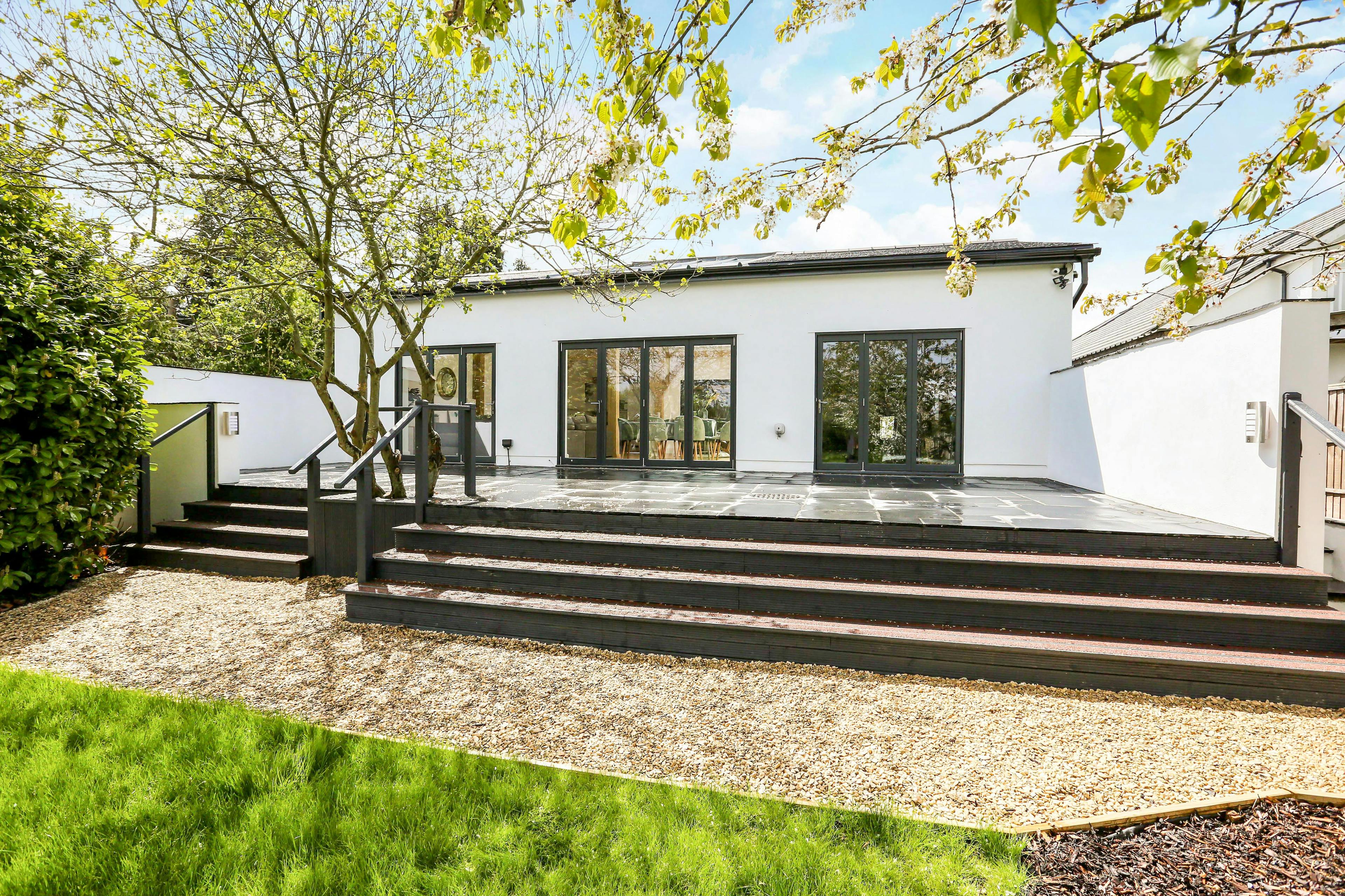 The back of a modern white house with steps leading down to a back garden