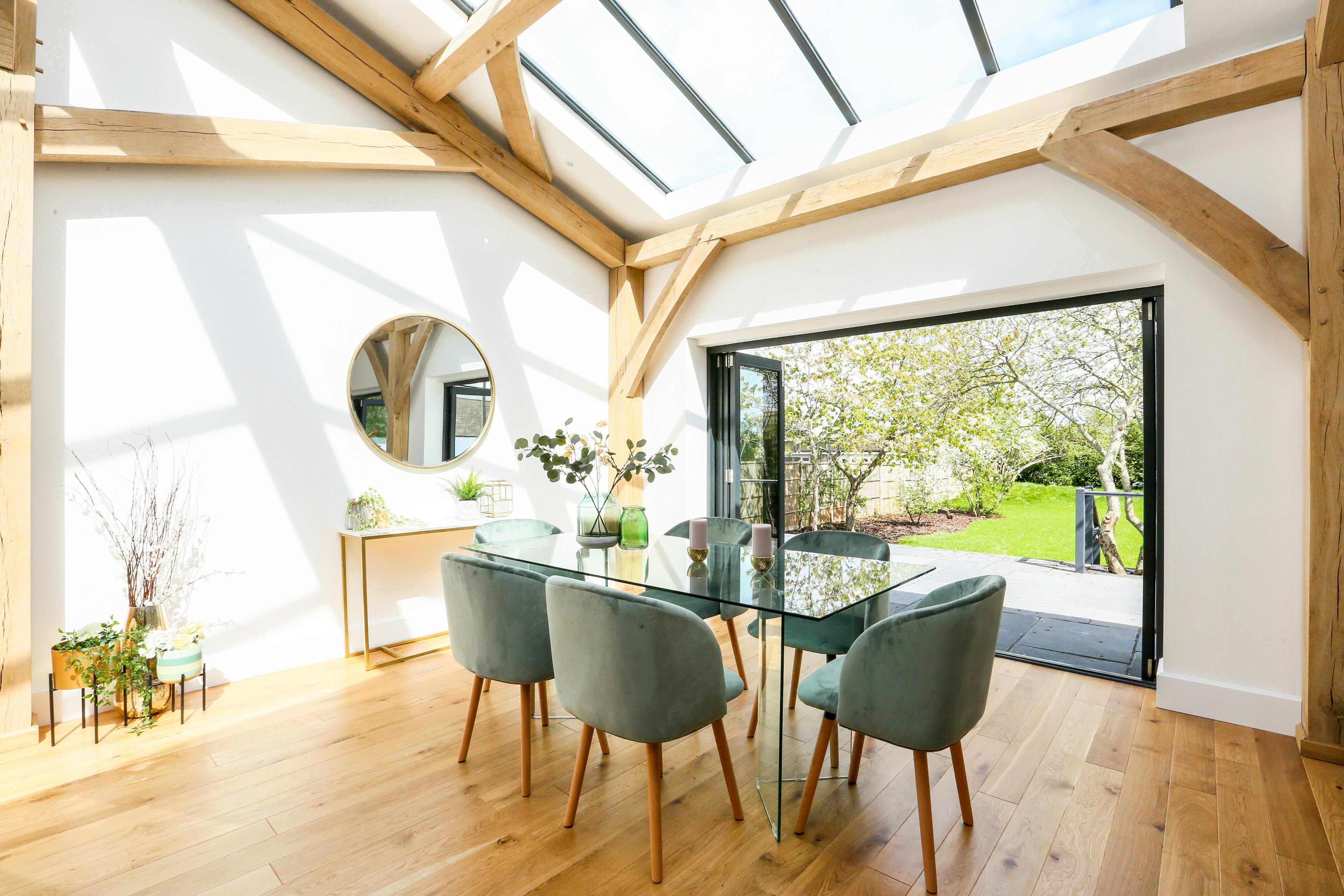 A light filled modern oak frame home with rooflights, showing a dining area with bifold doors opening out to the garden