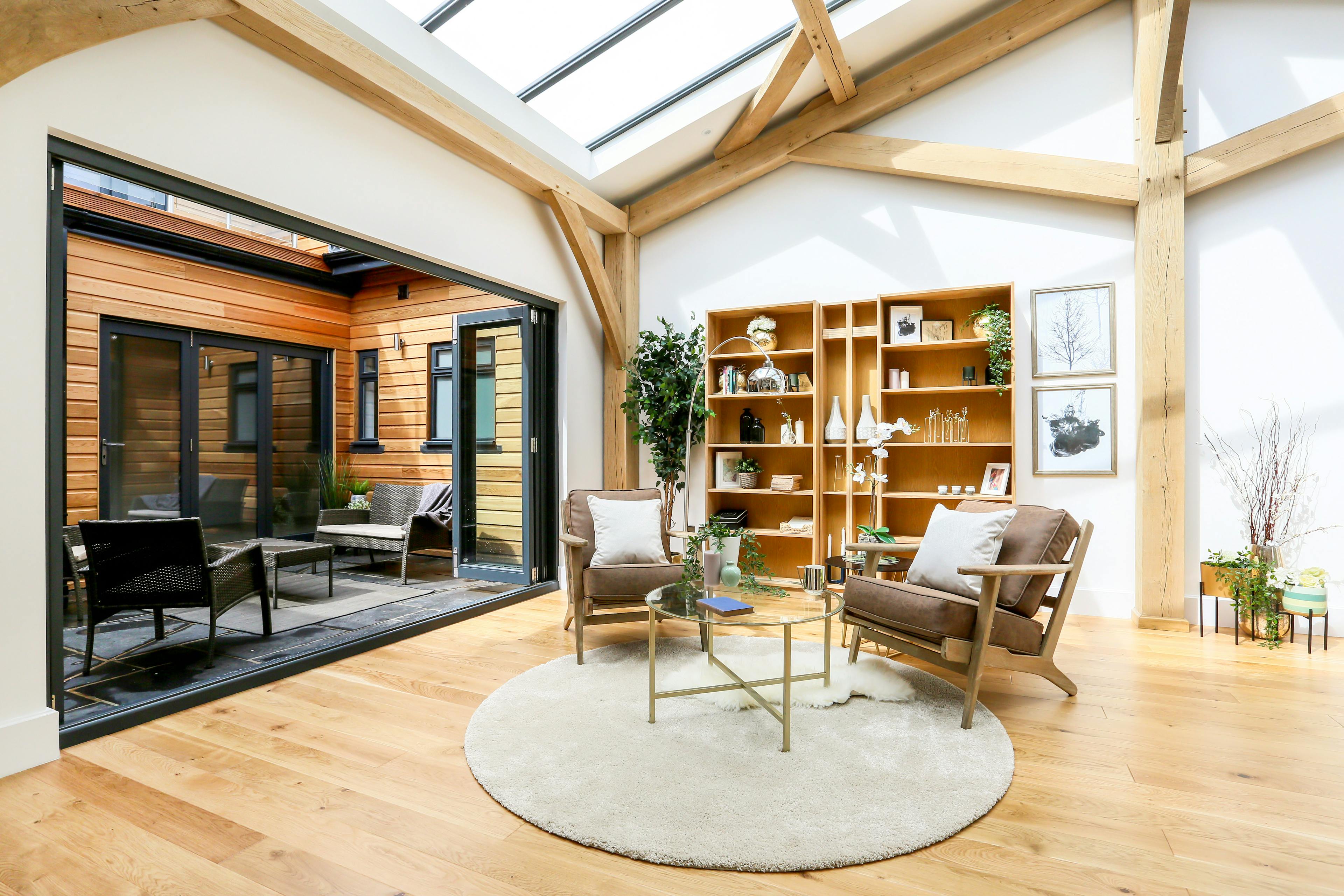 A light filled modern oak frame home with rooflights, showing an open plan living area with armchairs and an interior courtyard