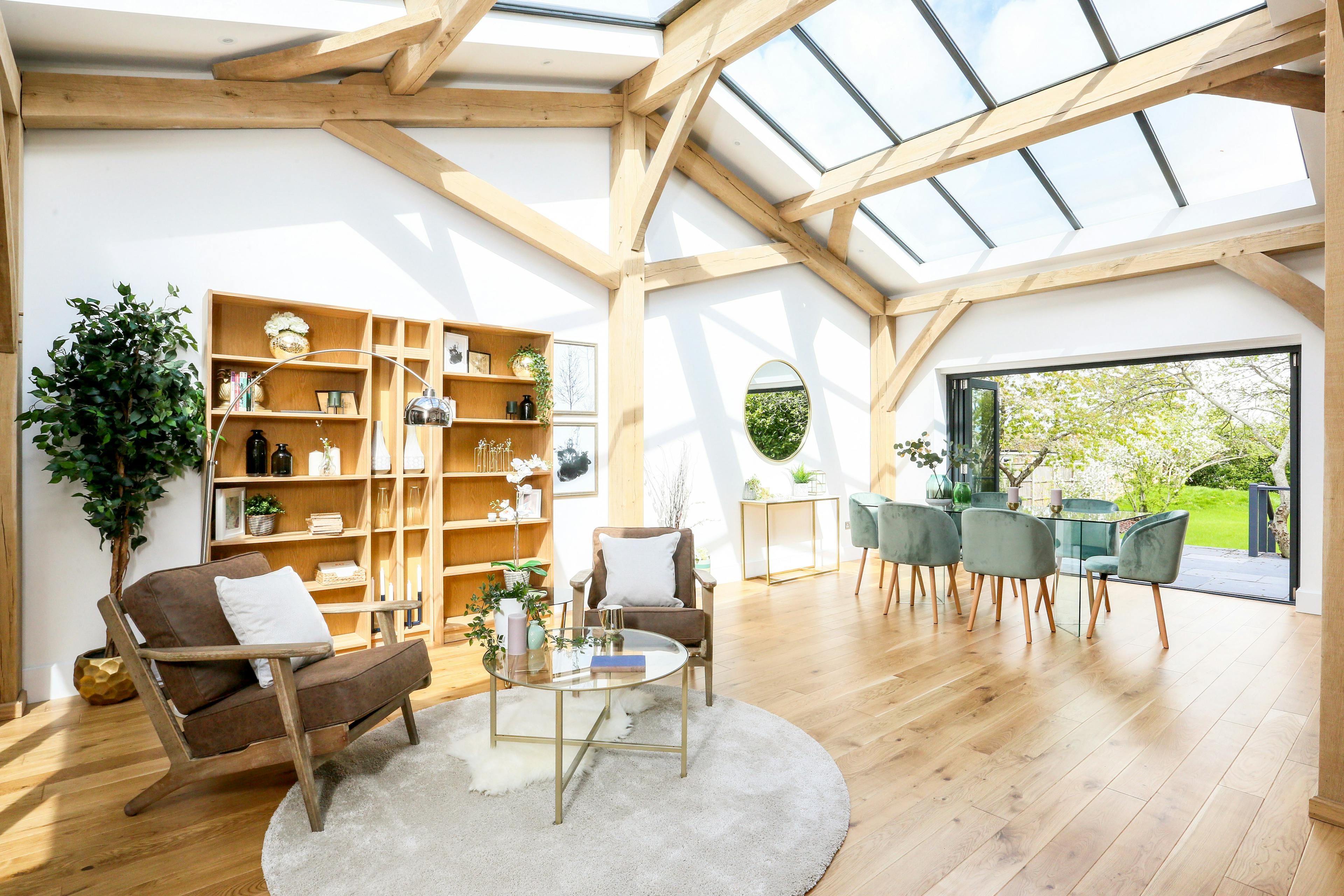 A light filled modern oak frame home with rooflights, showing an open plan living area with armchairs and dining area