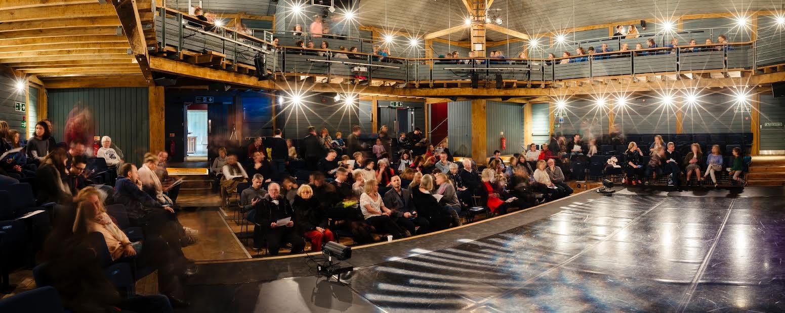 Interior of an oak frame theatre with an audience sat around the stage