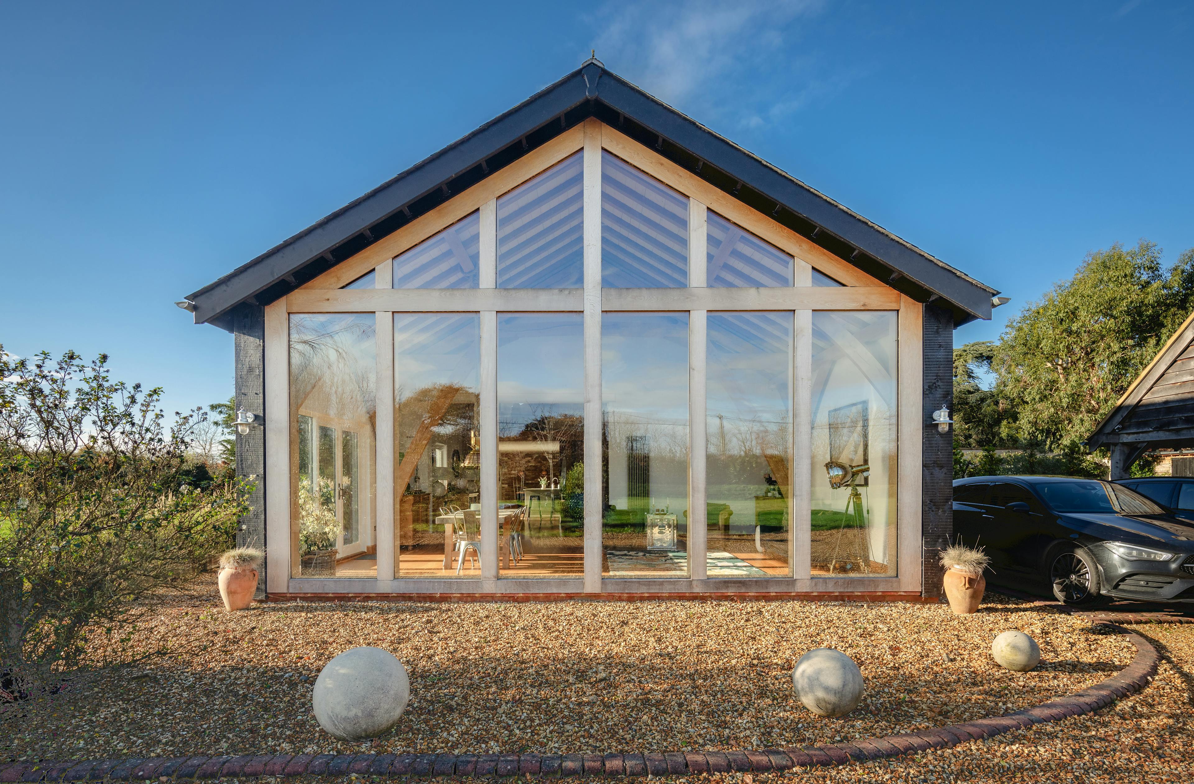 A gravel driveway with cars on it in front of an oak framed extension with a glazed gable