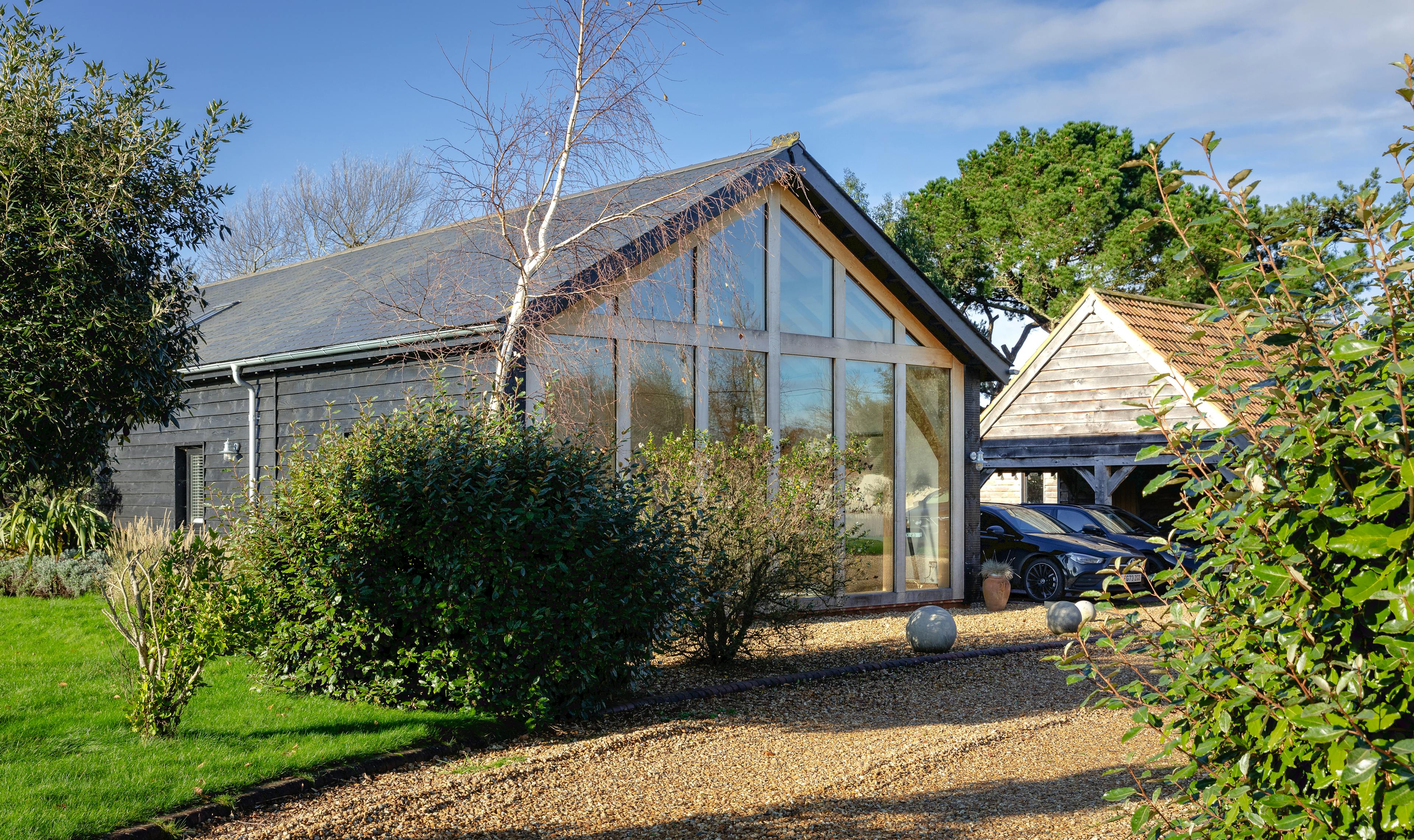 A gravel driveway with cars on it in front of an oak framed extension with a glazed gable