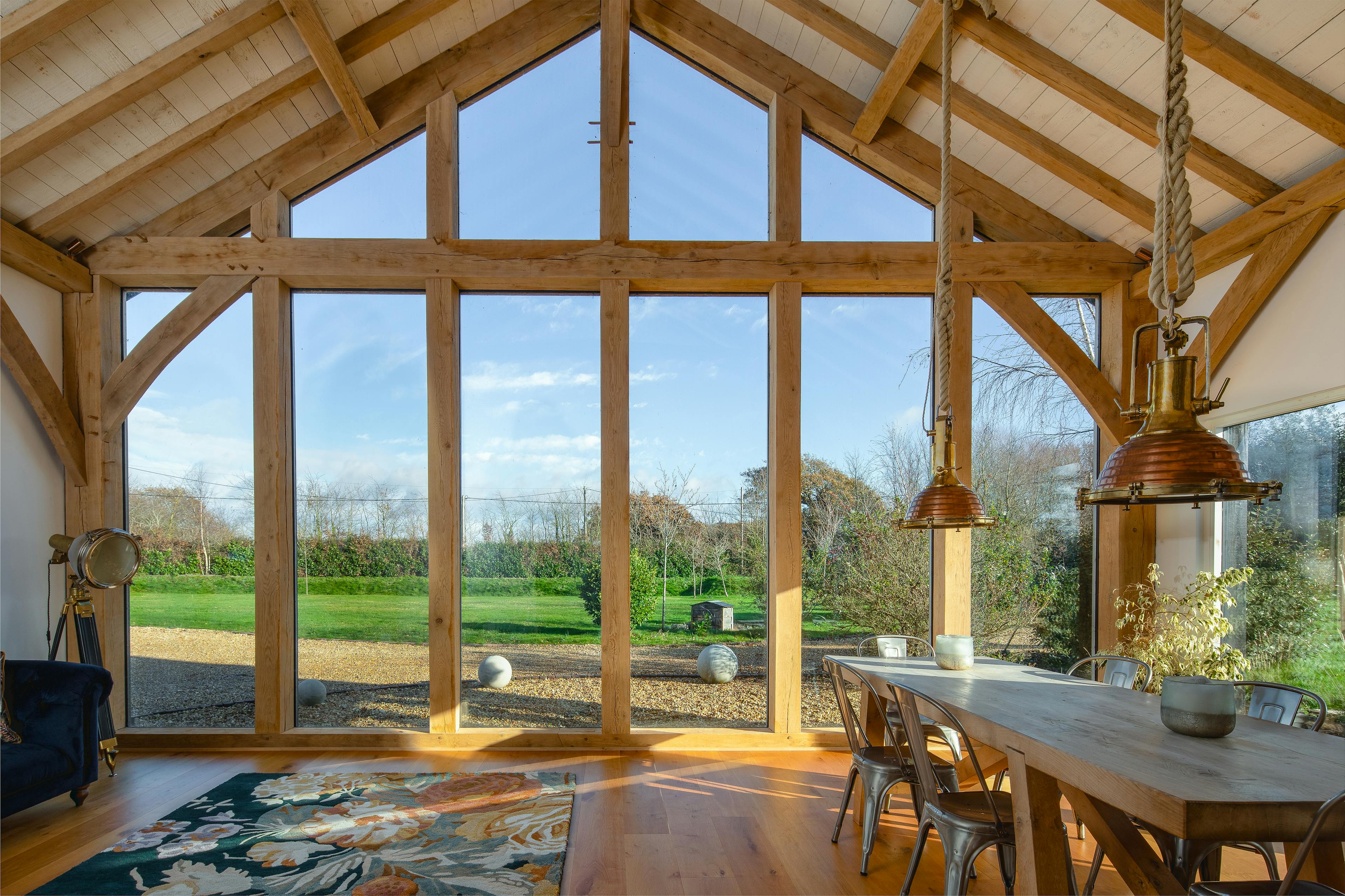 The view of a garden from inside an oak framed extension with a glazed gable, with a table and chairs in the foreground