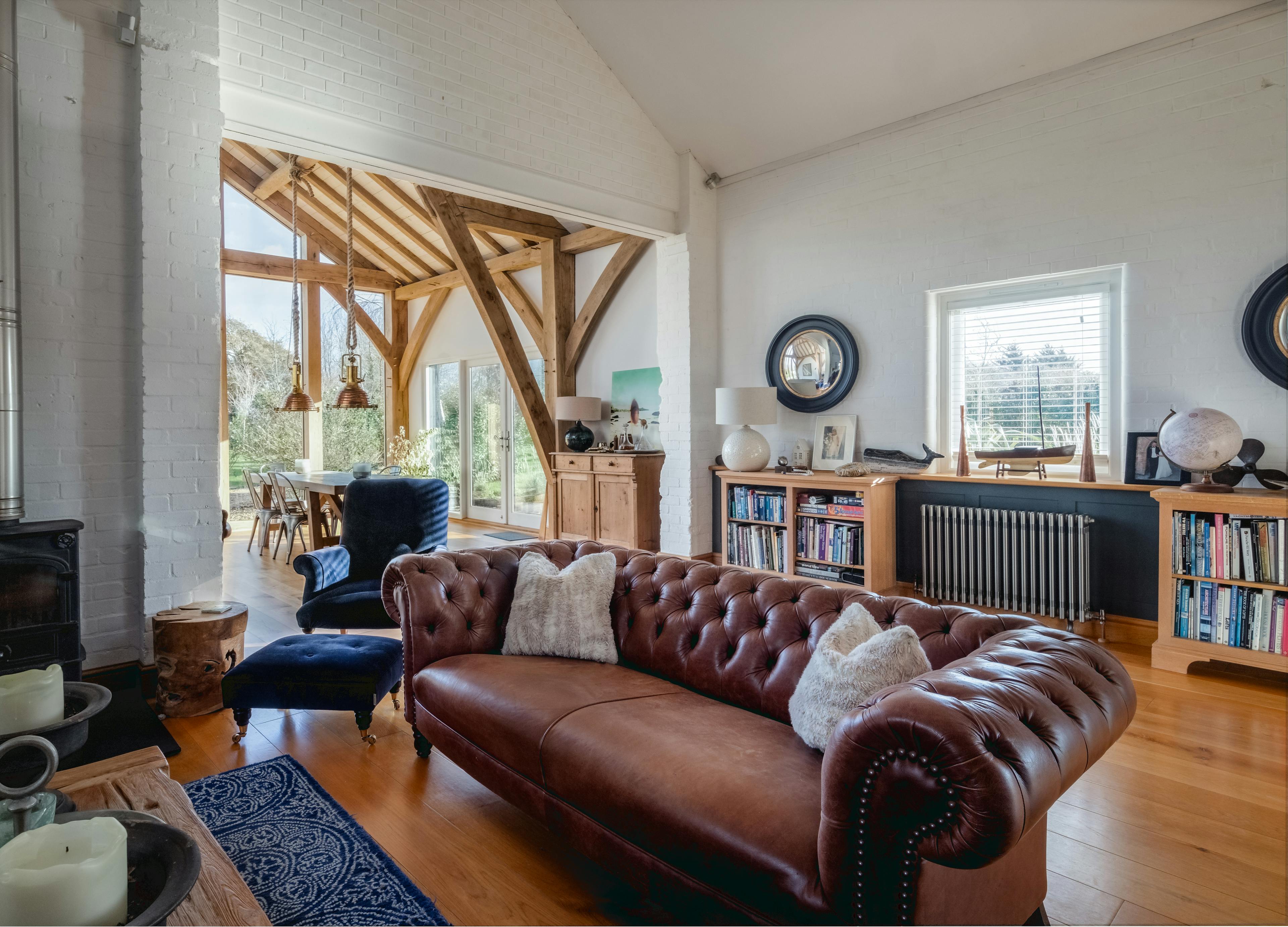 A large sitting room with brown leather sofa in the foreground and oak framed extension in the background