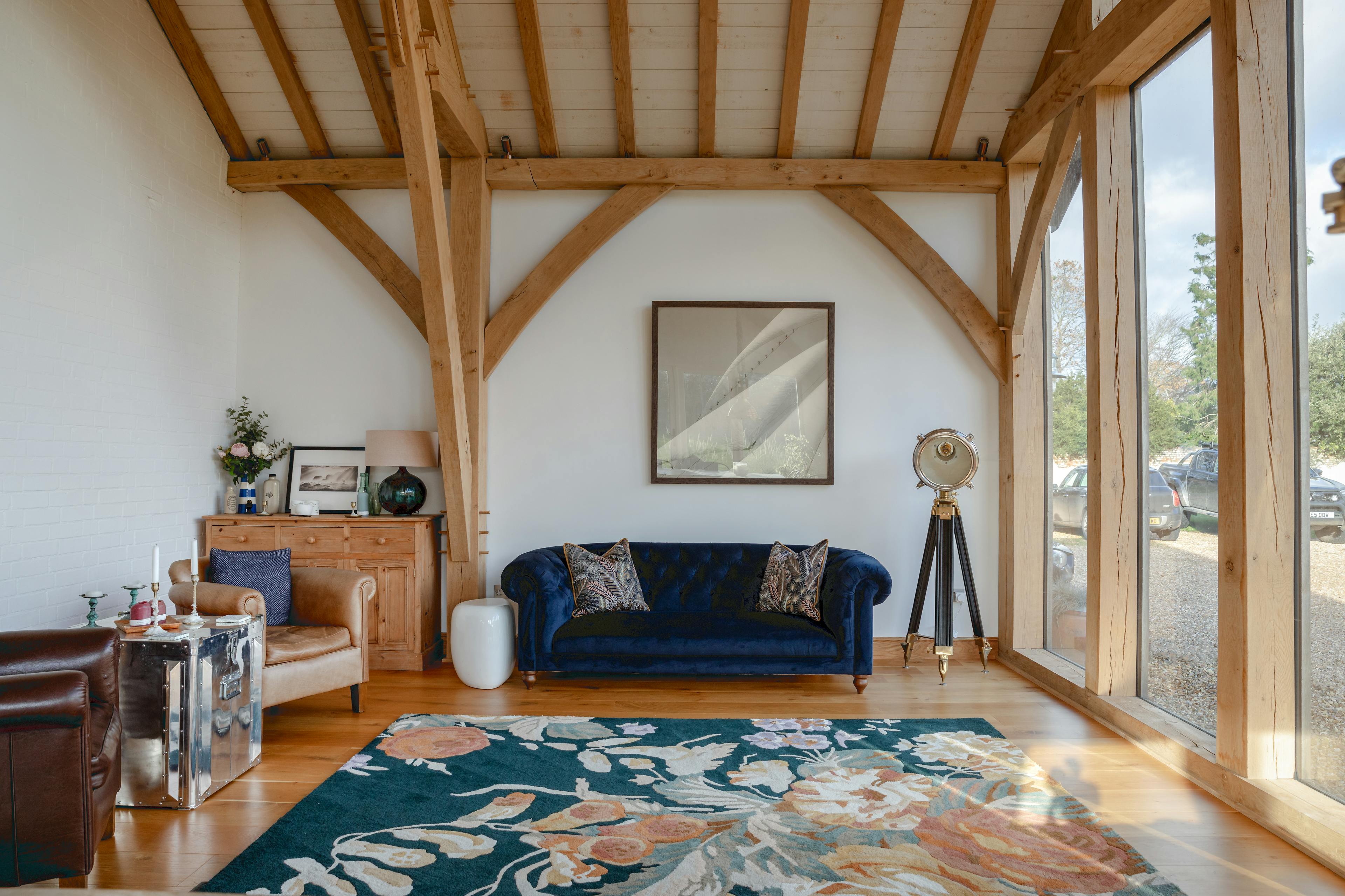 A sofa an armchairs in a corner of an oak framed extension with a glazed gable