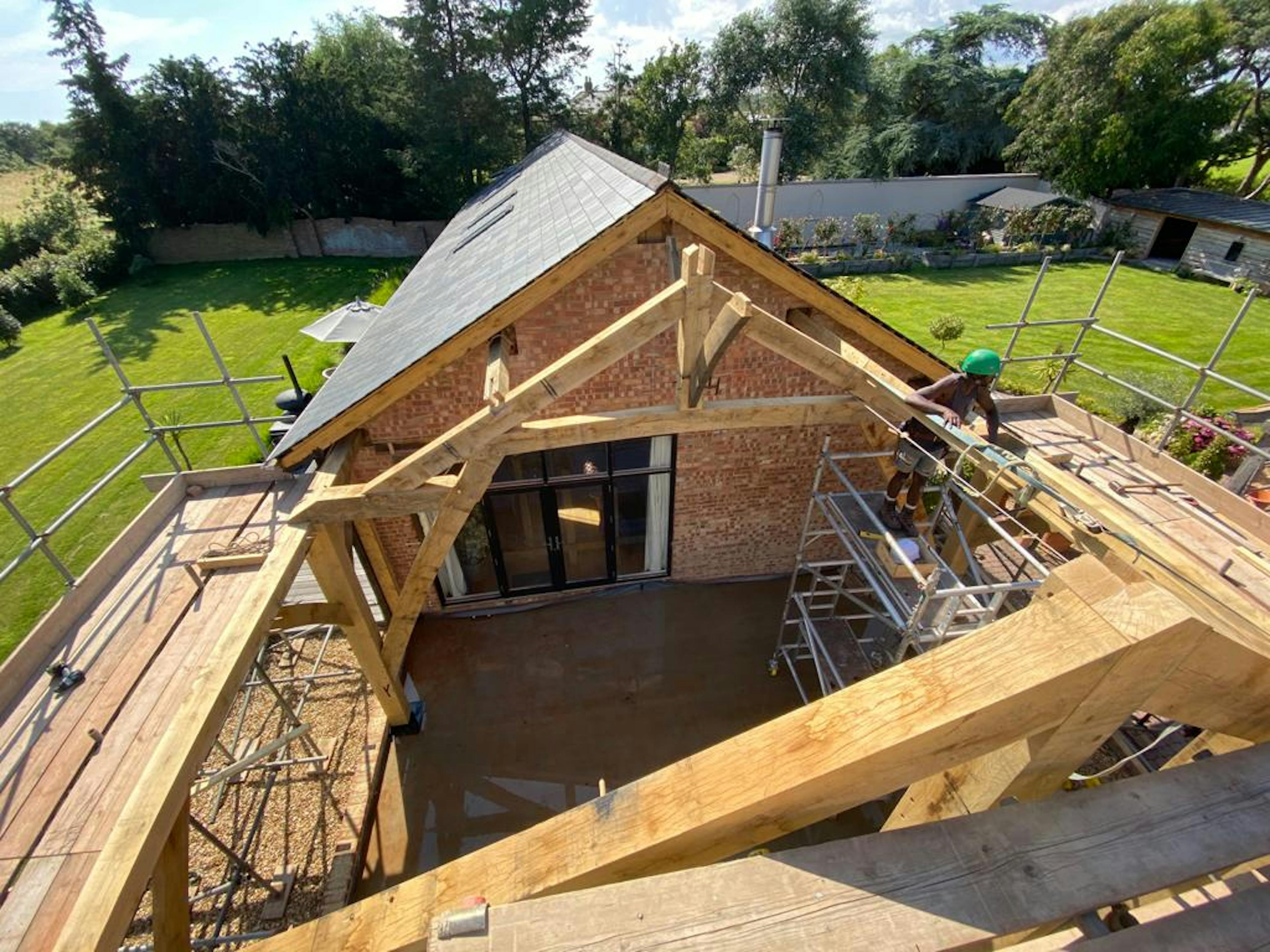 A carpenter in a hard hat works on installing an oak frame on a building site