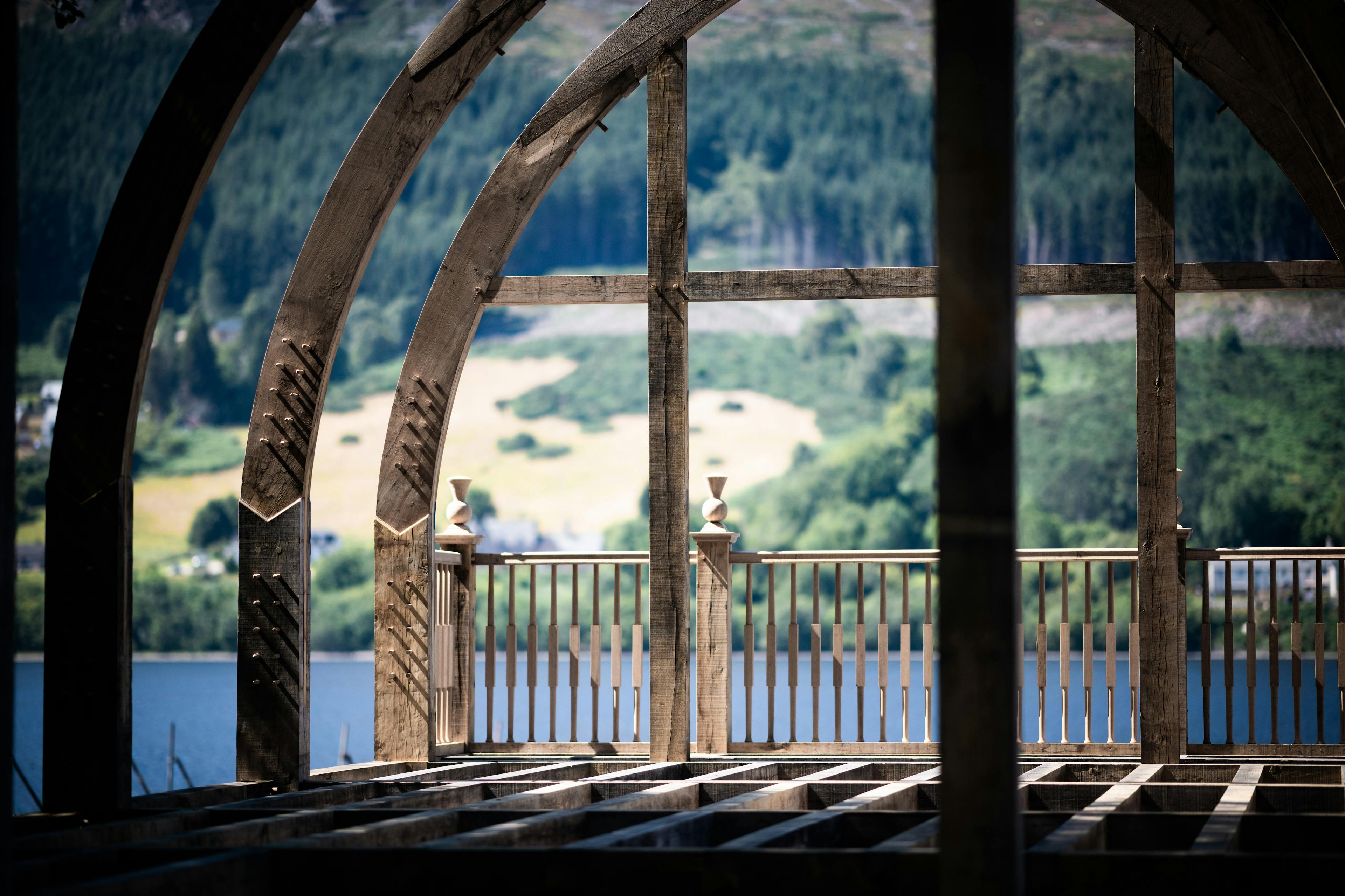 The other side of the loch show through the oak frame of a timber boathouse on loch ness with a curved roof during construction