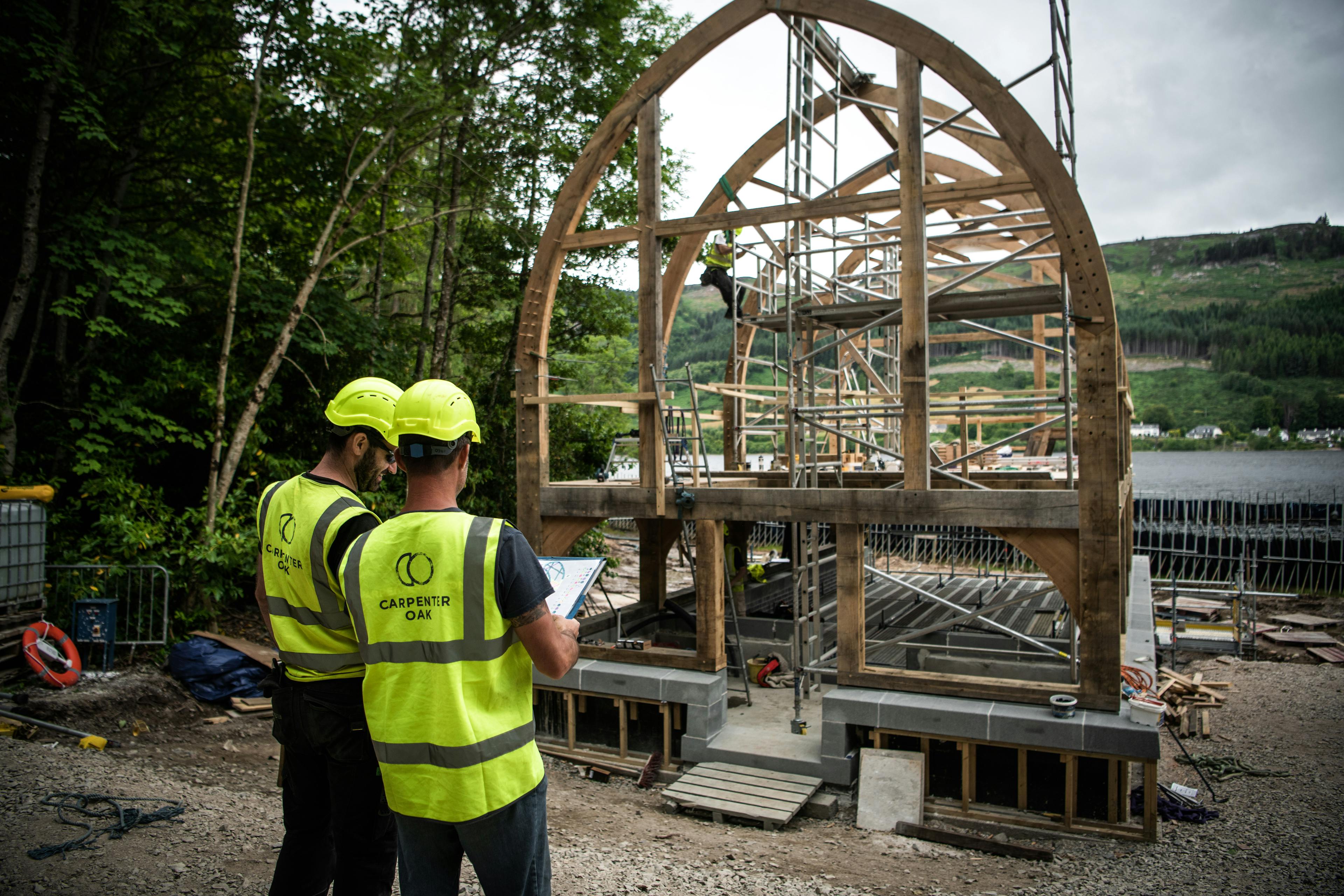 Carpenters install an oak framed boathouse with a curved roof by a lake
