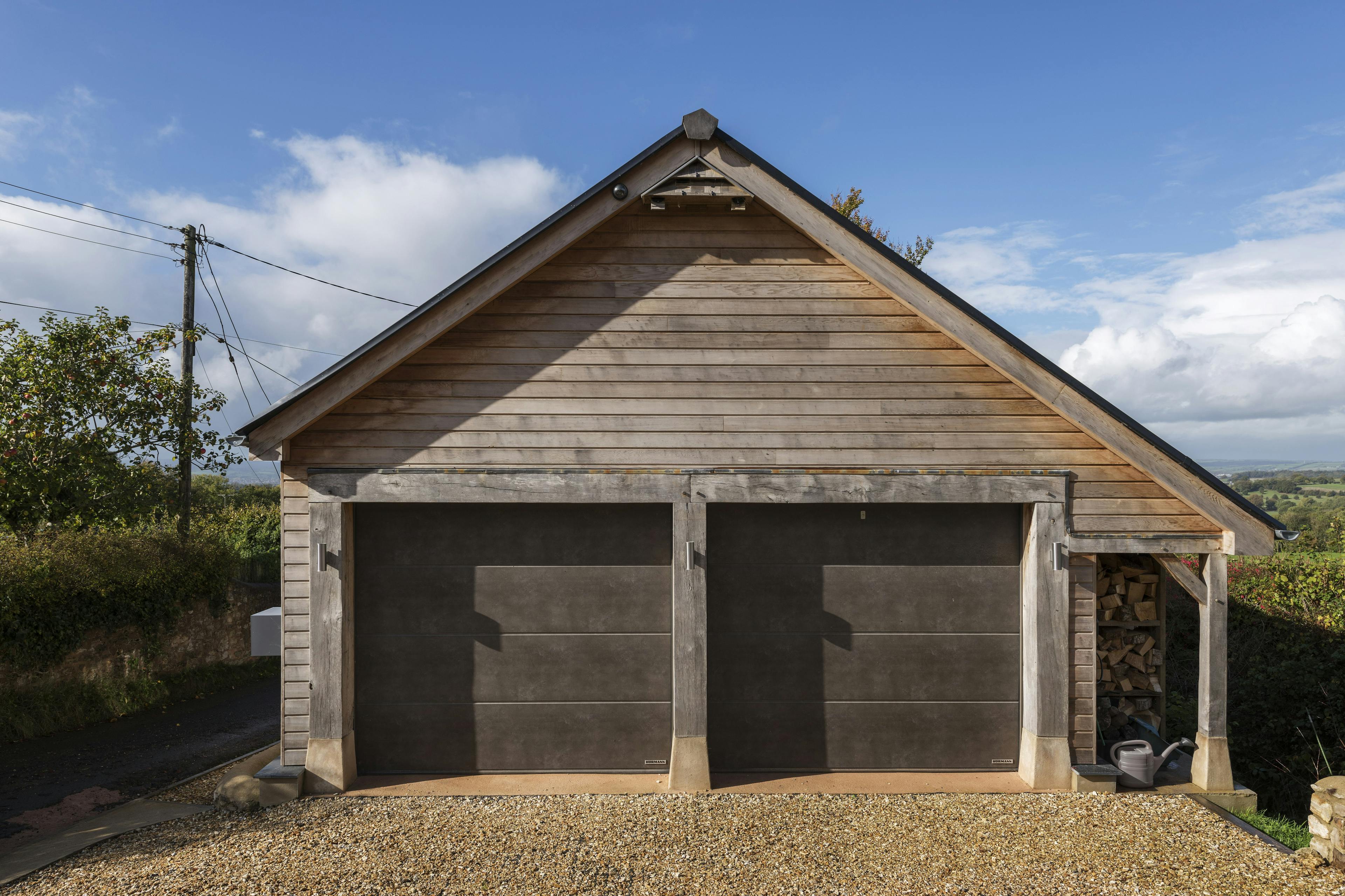 A timber clad garage with double doors and an A frame sloped roof