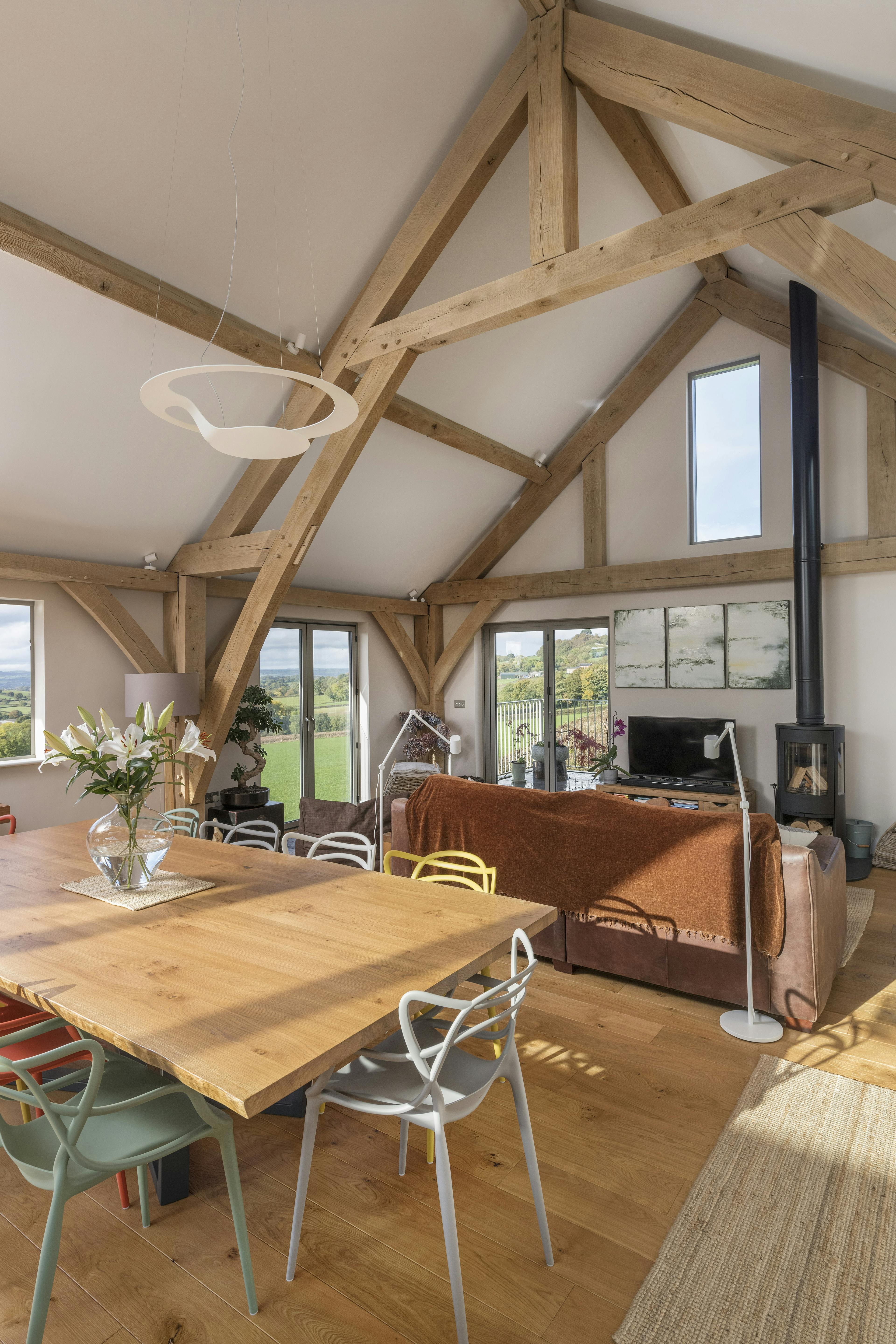 A dining table, sitting area and log burner in a vaulted oak framed open plan living room