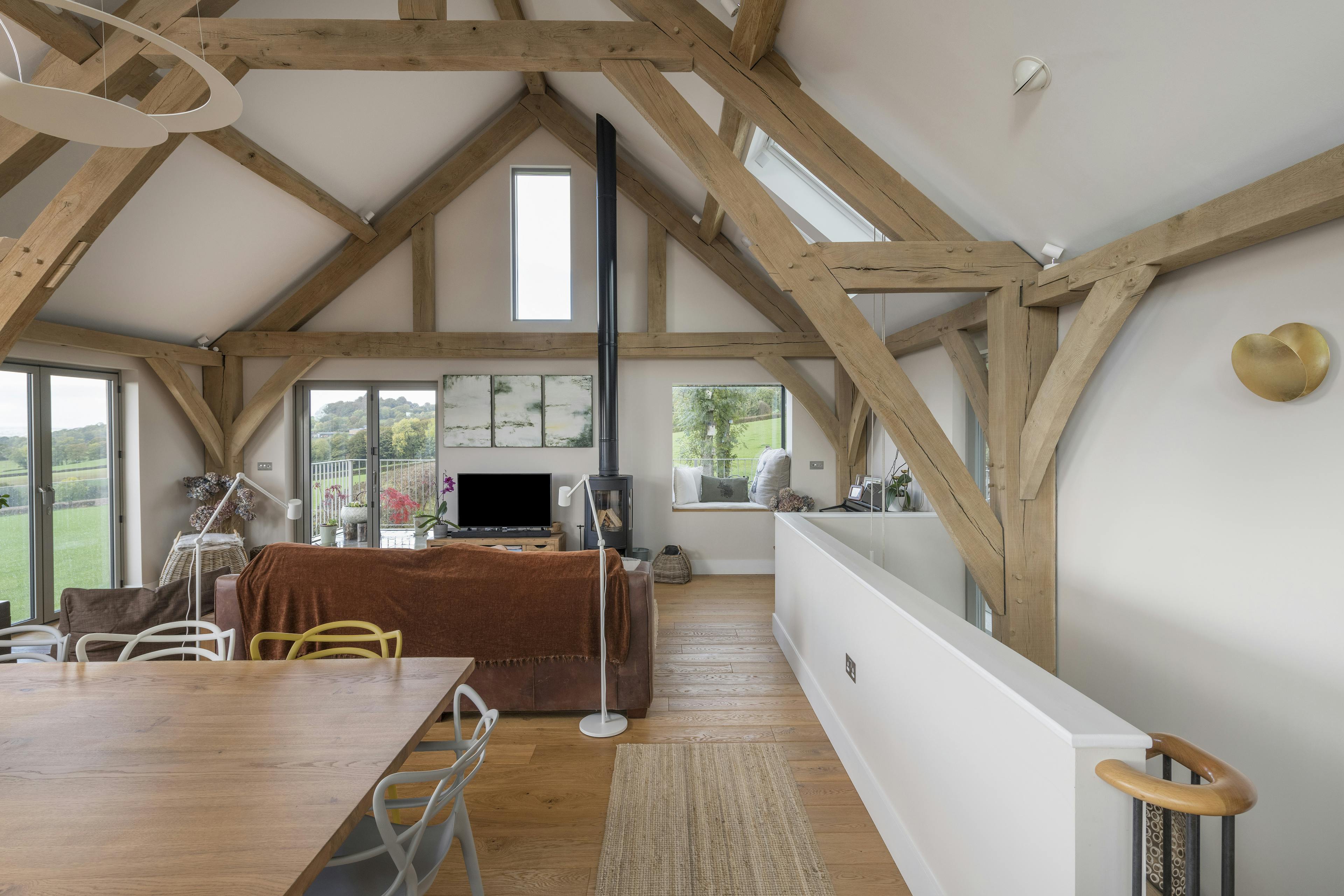 A dining table, sitting area and log burner in a vaulted oak framed open plan living room