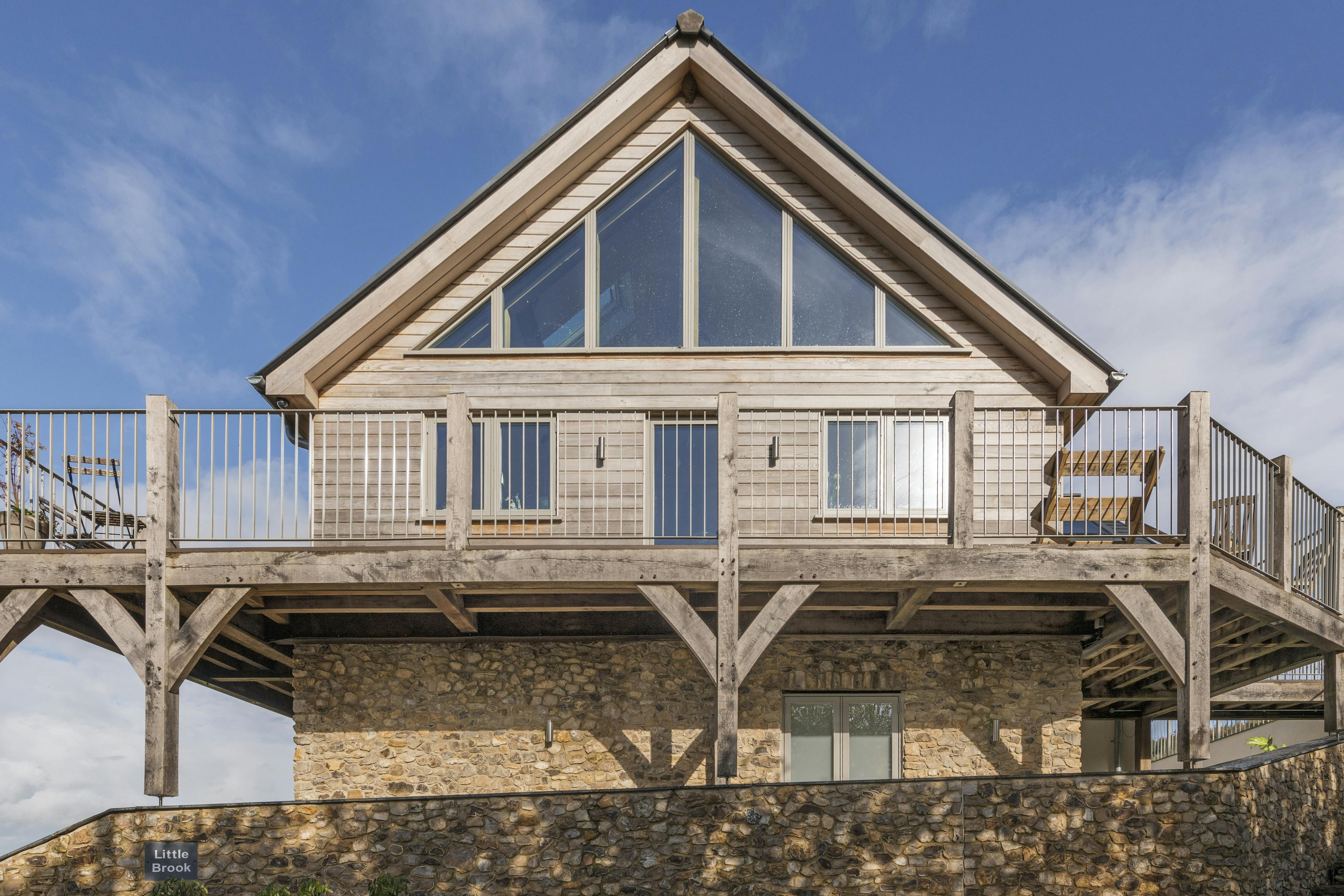 A blue sky behind the glazed gable of a timber clad oak framed house with oak balconies wrapping round