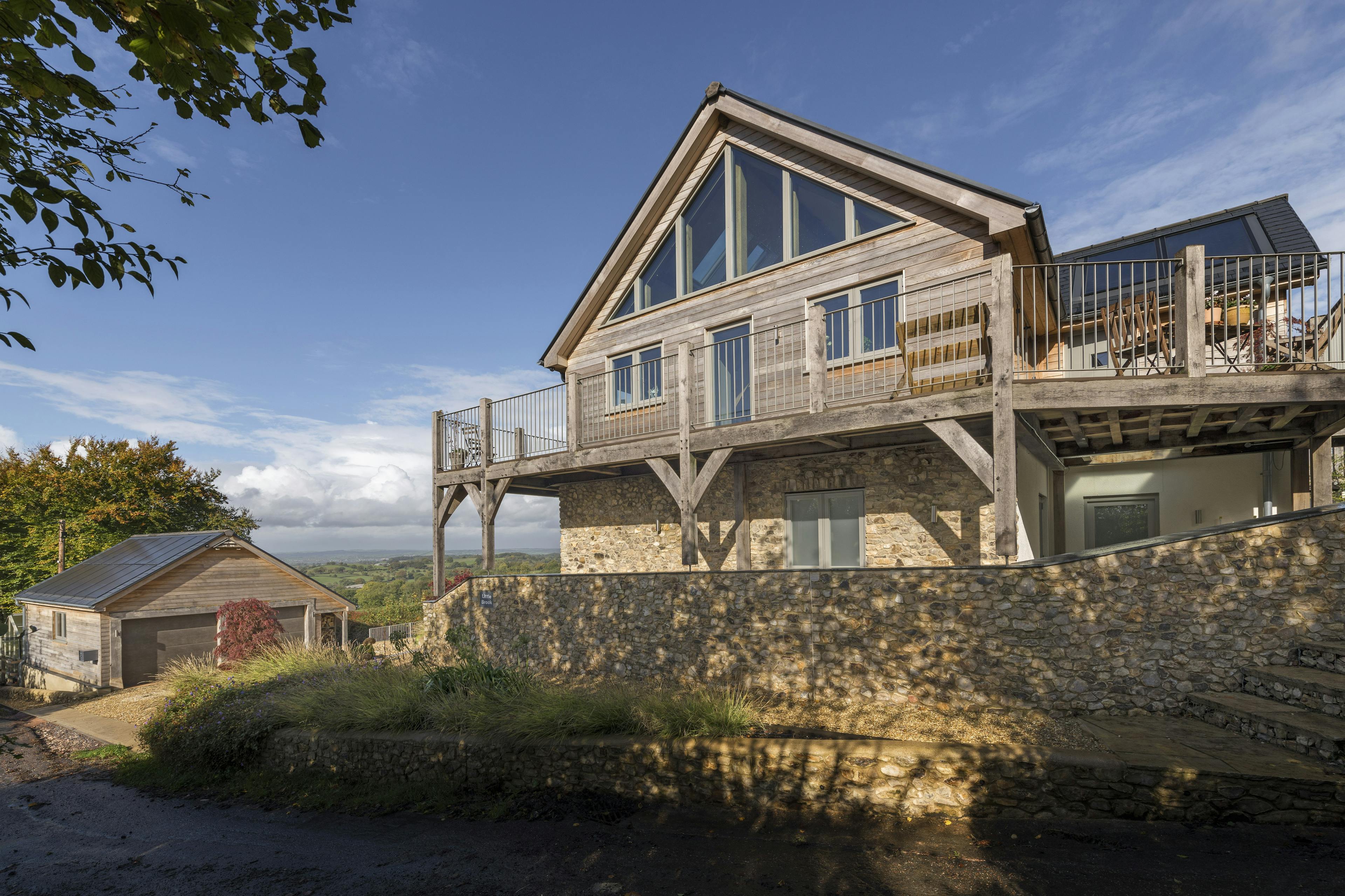 A glazed gable end of a timber clad oak framed house with oak balconies wrapping round, and a double garage to the site