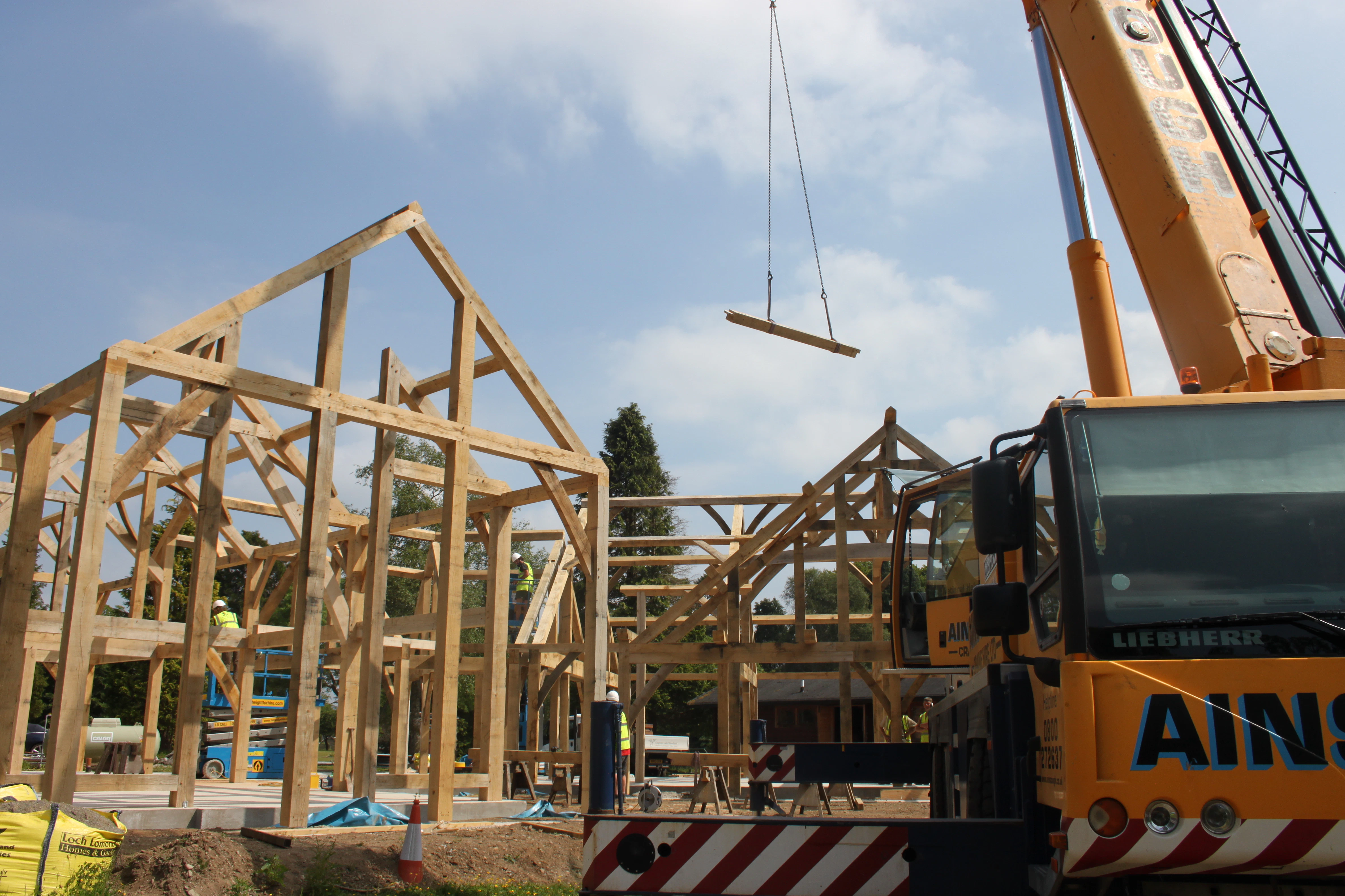 On a construction site an orange crane lifts a piece of oak during the installation of two oak framed houses 