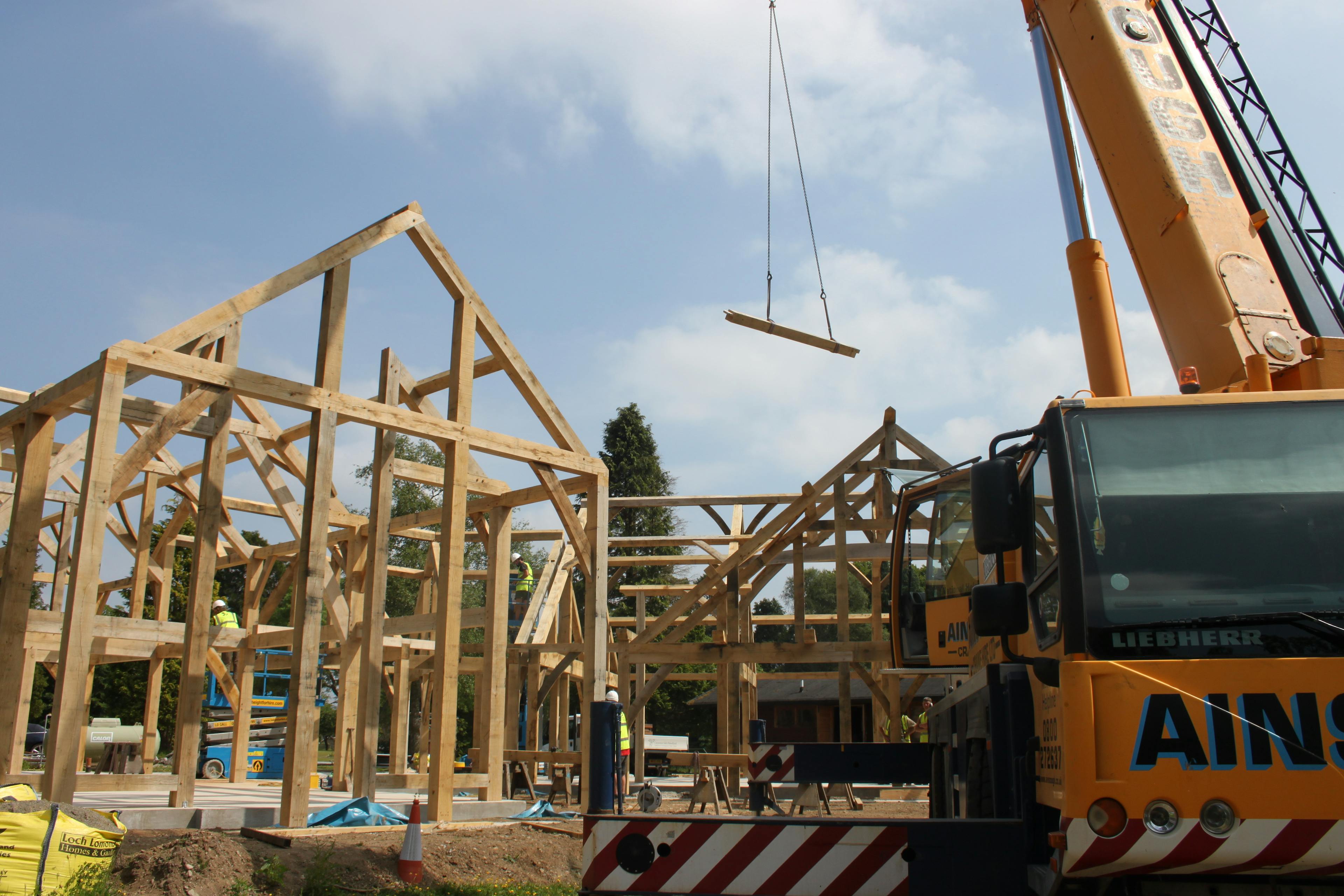 On a construction site an orange crane lifts a piece of oak during the installation of two oak framed houses 
