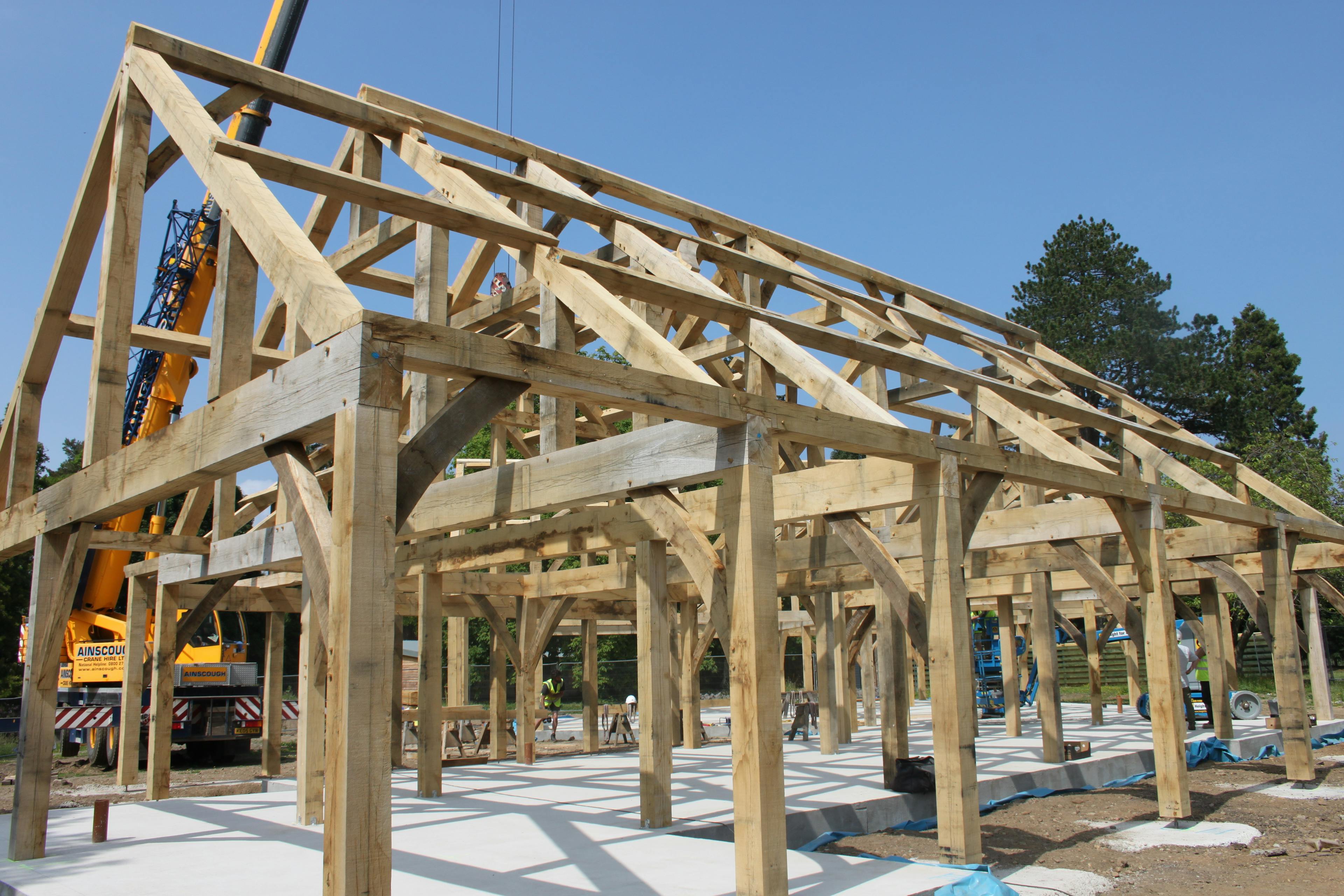 On a construction site an oak frame is installed by a yellow crane