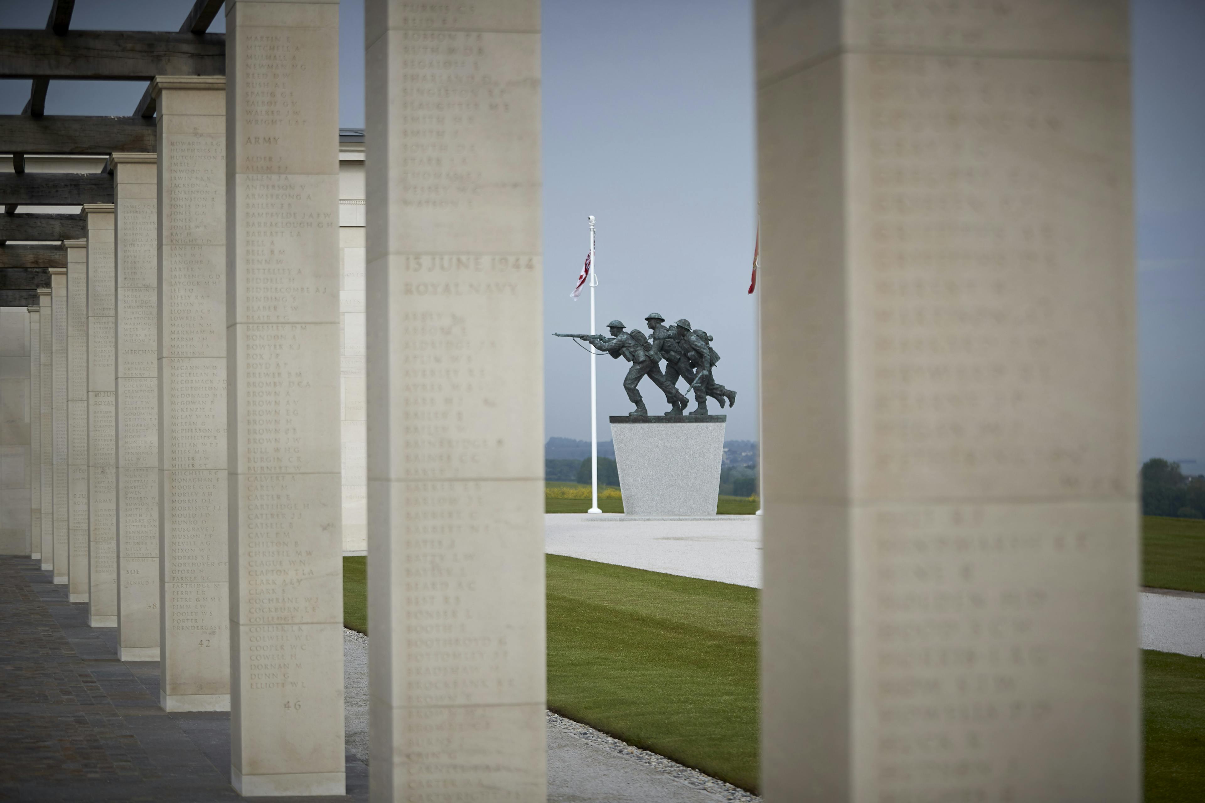 A statue of allied forces can be seen between stone columns with an oak pergola at the British Normandy Memorial