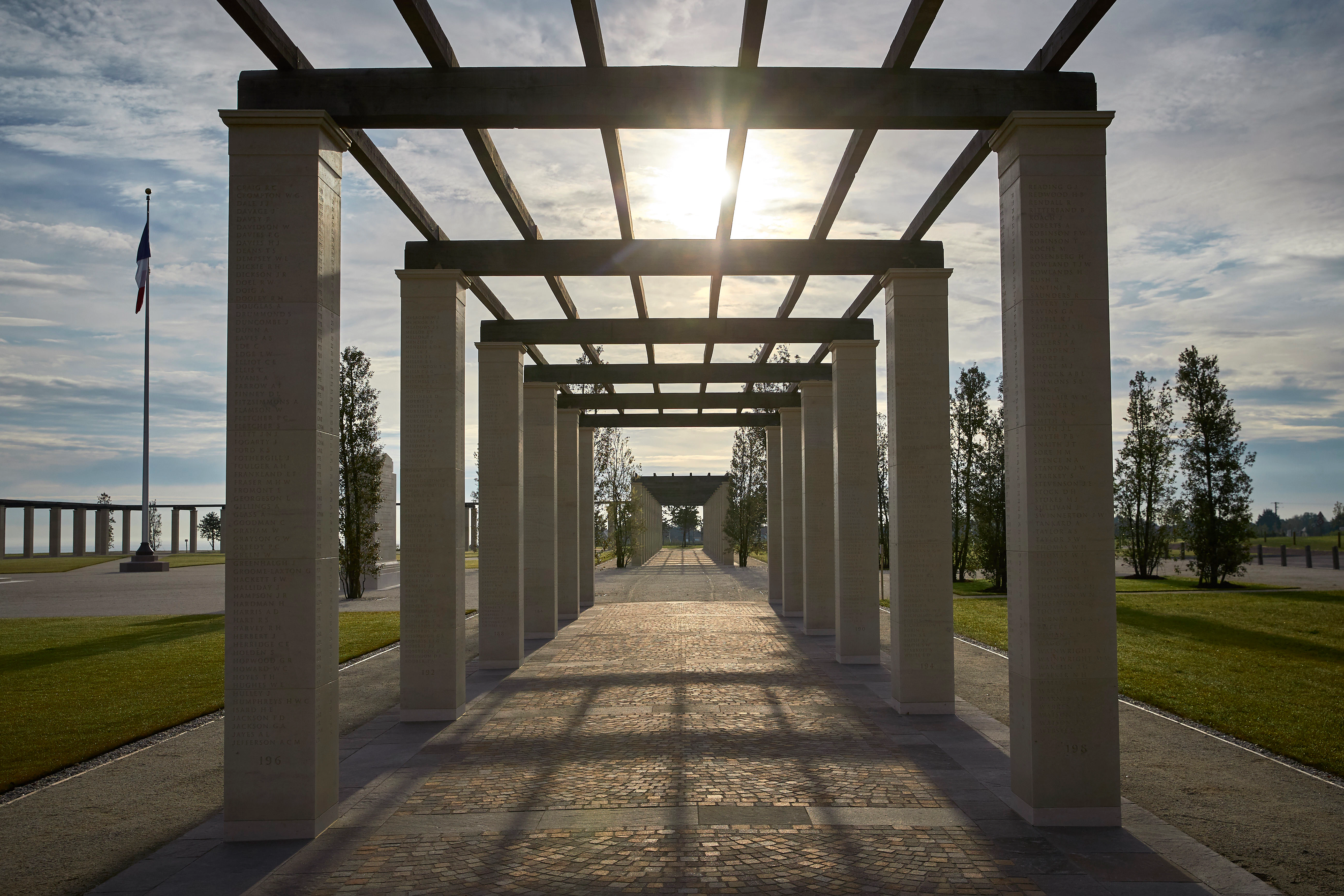 The sun sets behind stone columns with an oak pergola at the British Normandy Memorial