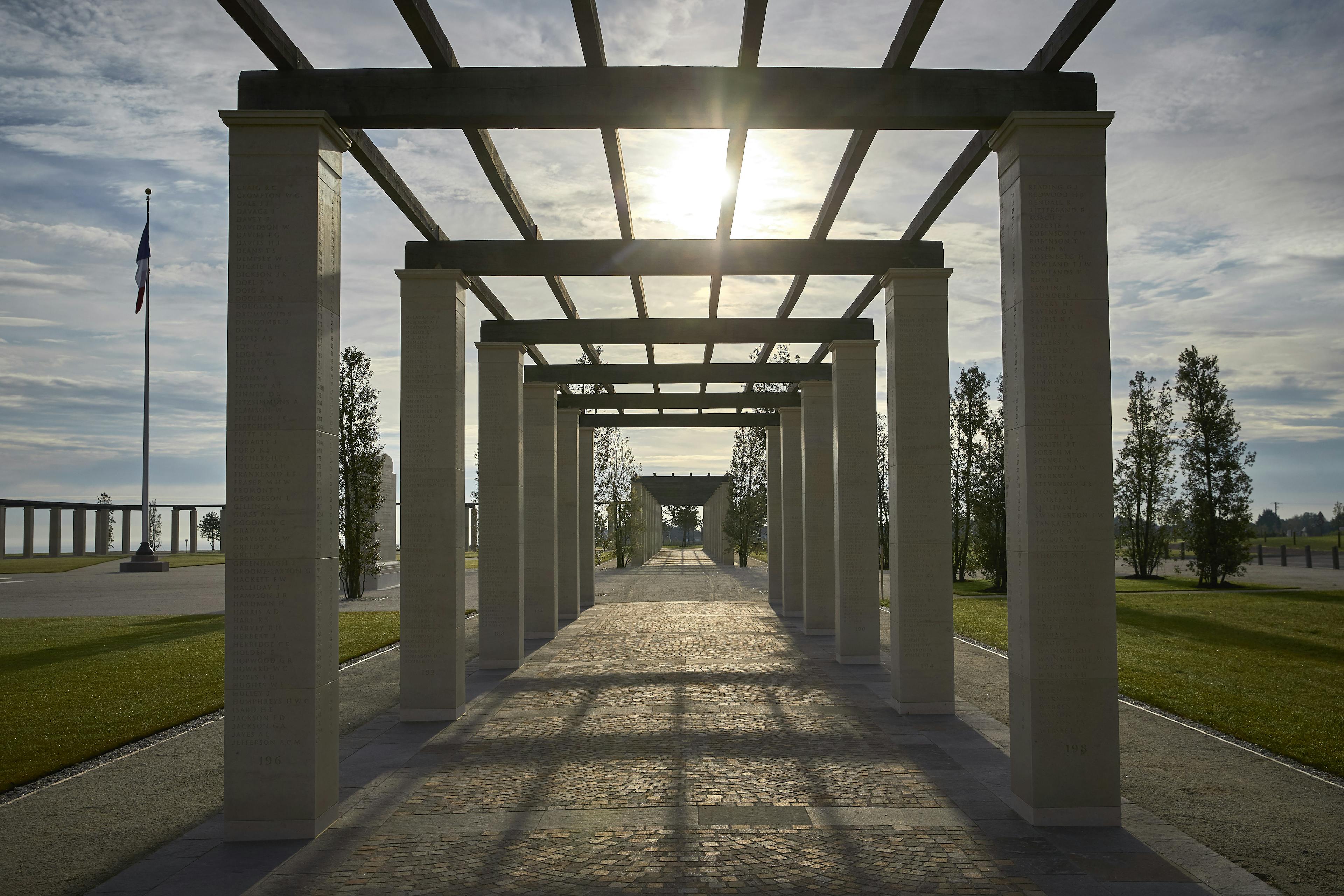 The sun sets behind stone columns with an oak pergola at the British Normandy Memorial