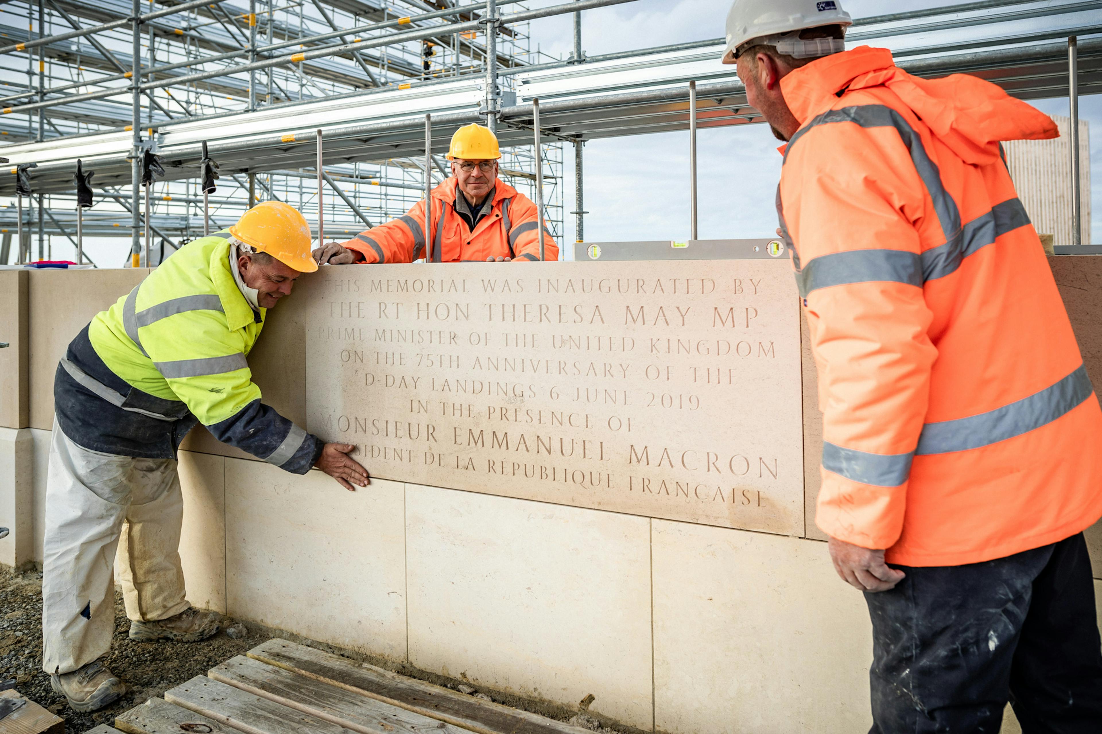 Construction workers on scaffolding lay stone blocks to make a column