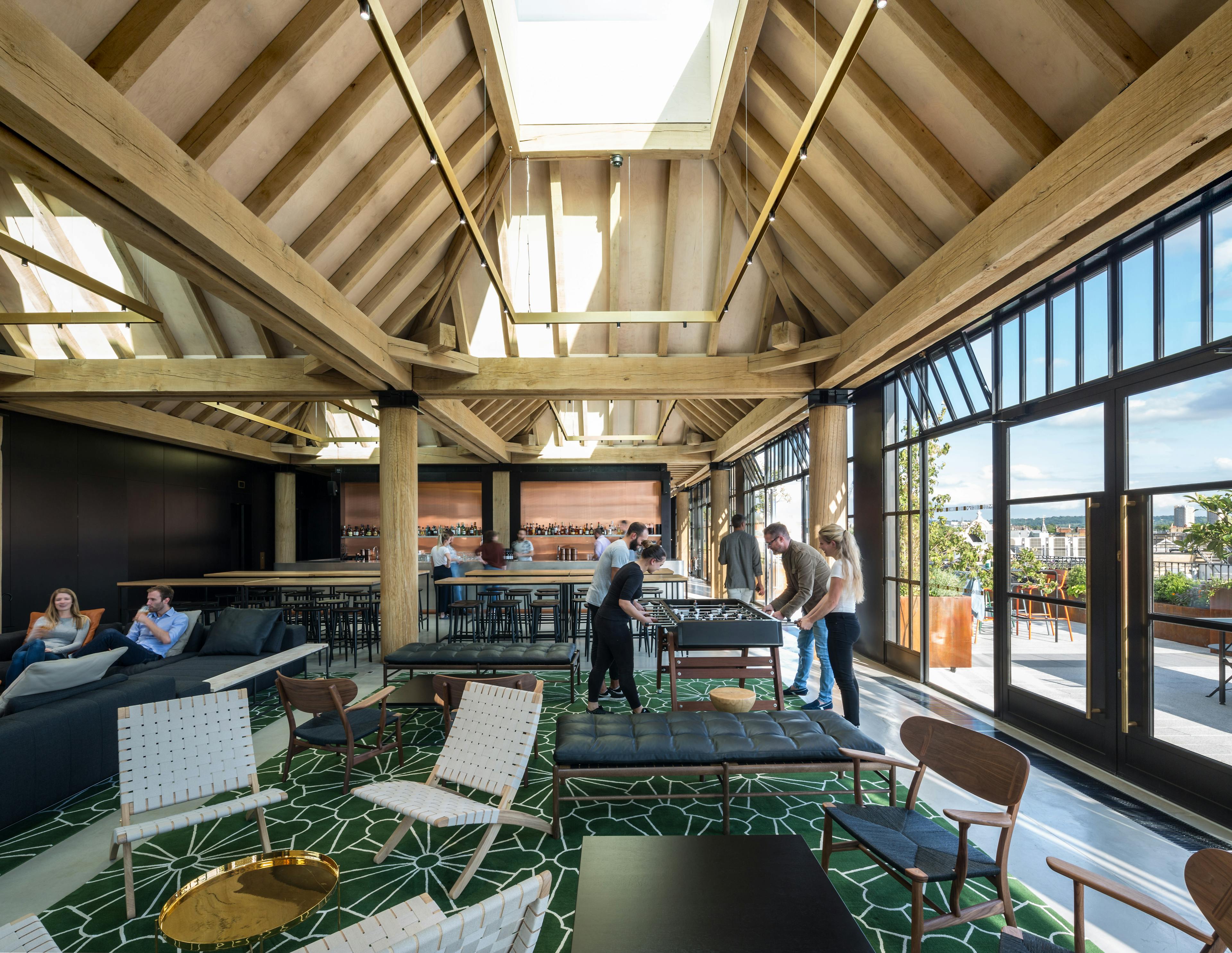 Oak frame lanterns link to create a rooftop bar with customers sat at tables and sofas and playing football table