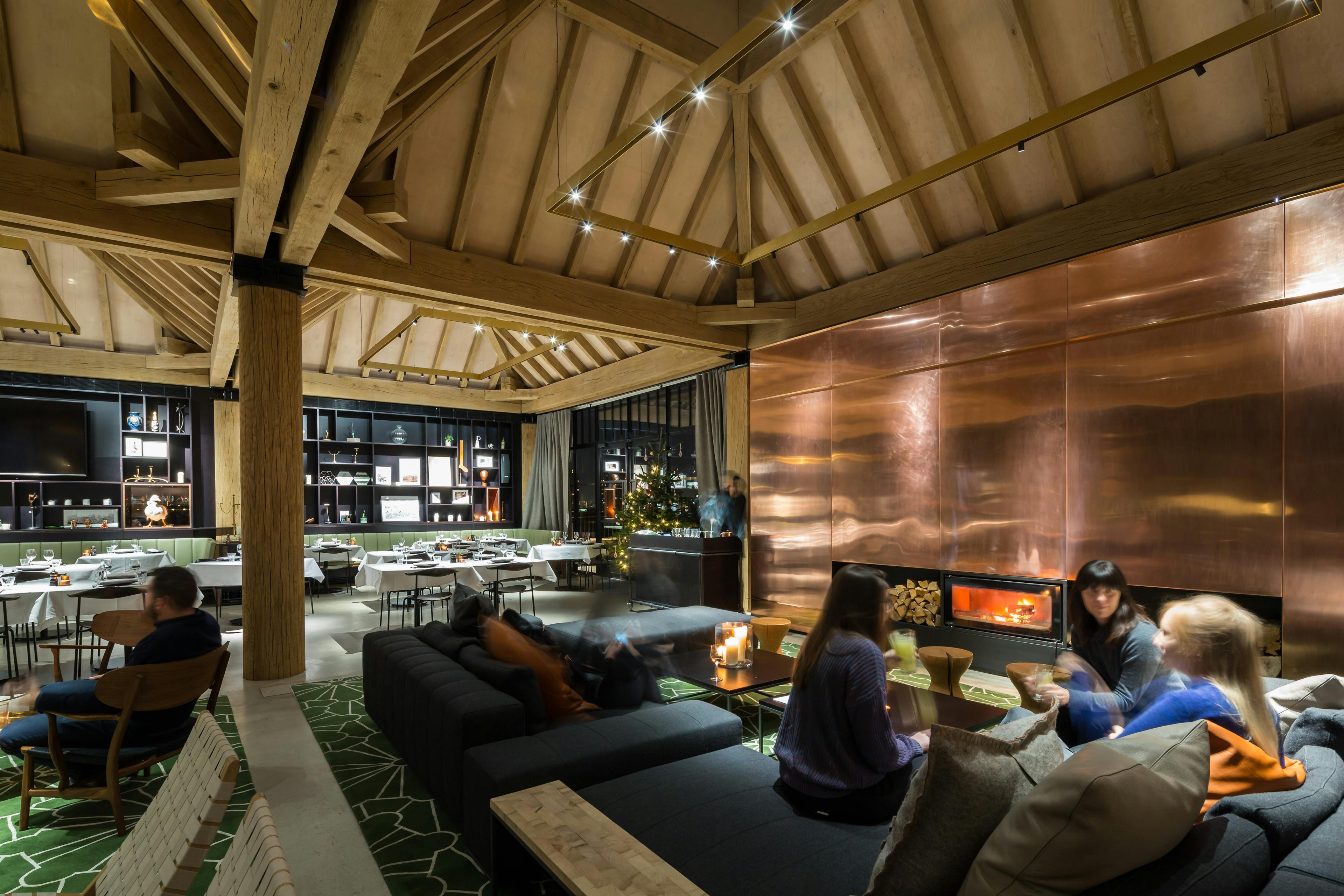 Oak frame lanterns link to create a rooftop bar with customers sat on sofas and a log burner burns brightly