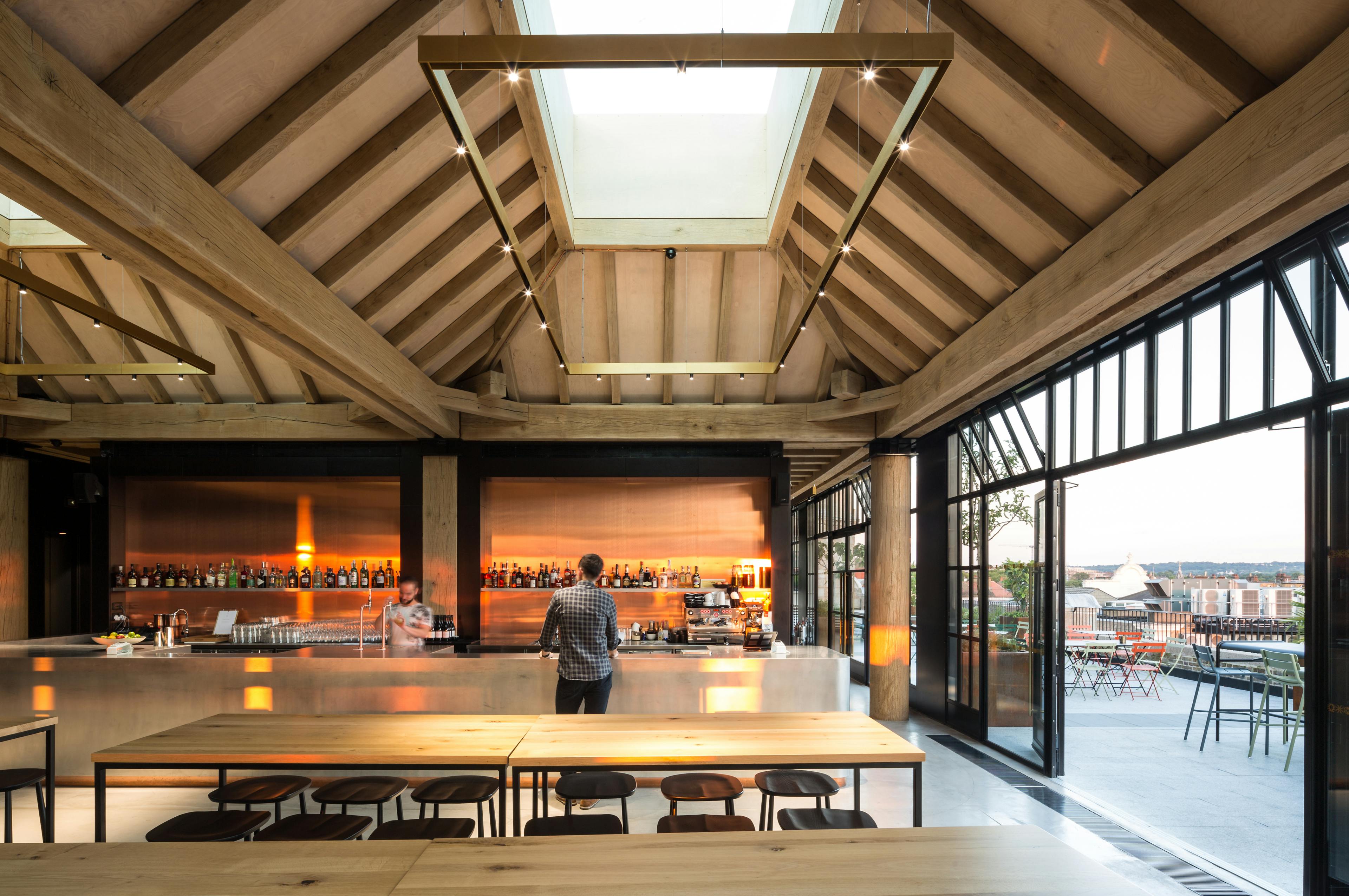 Oak frame lanterns link to create a rooftop bar with customer standing at a bar