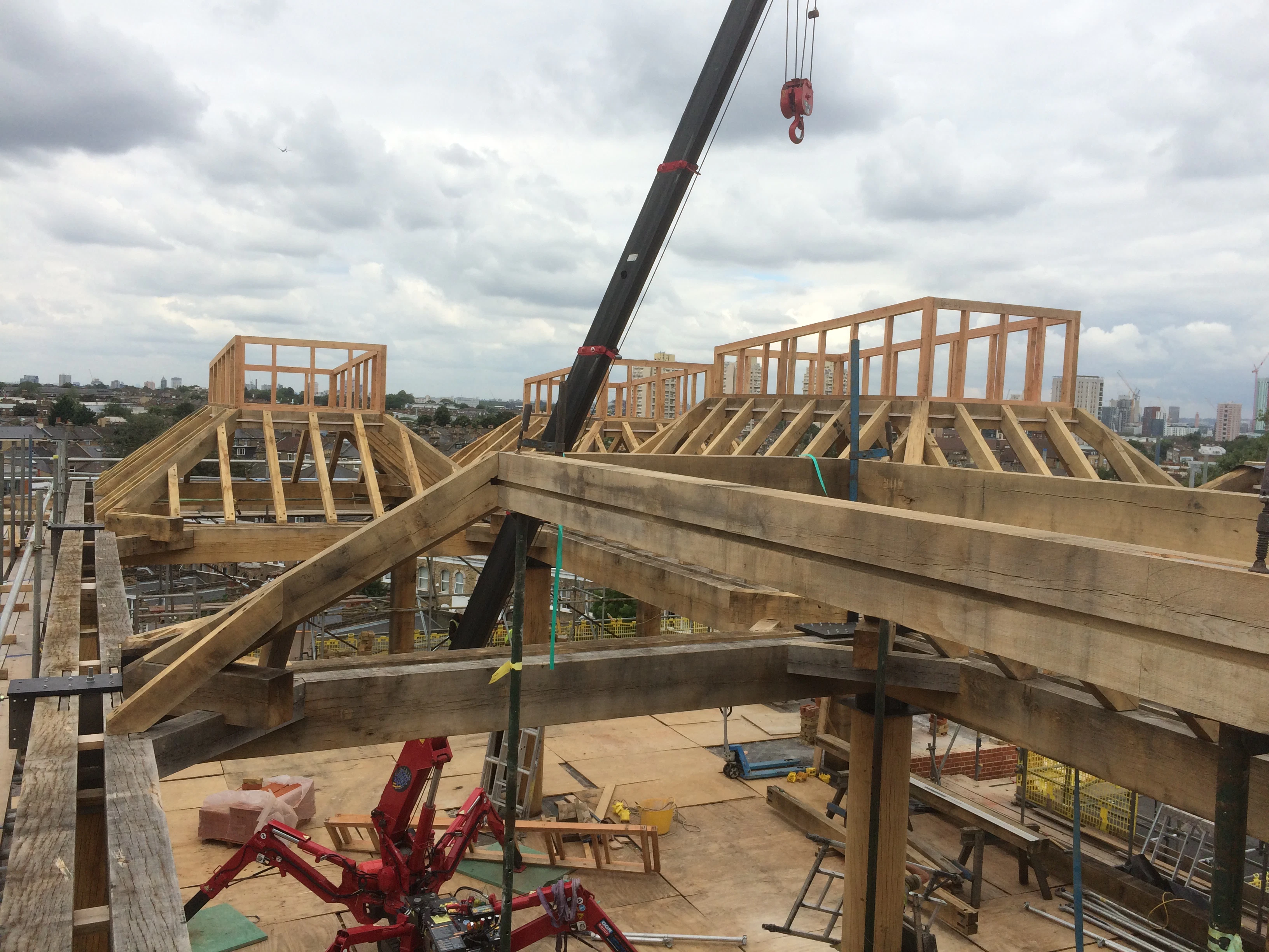 Oak frame lanterns are put in place by a red spider crane on a rooftop in a city 