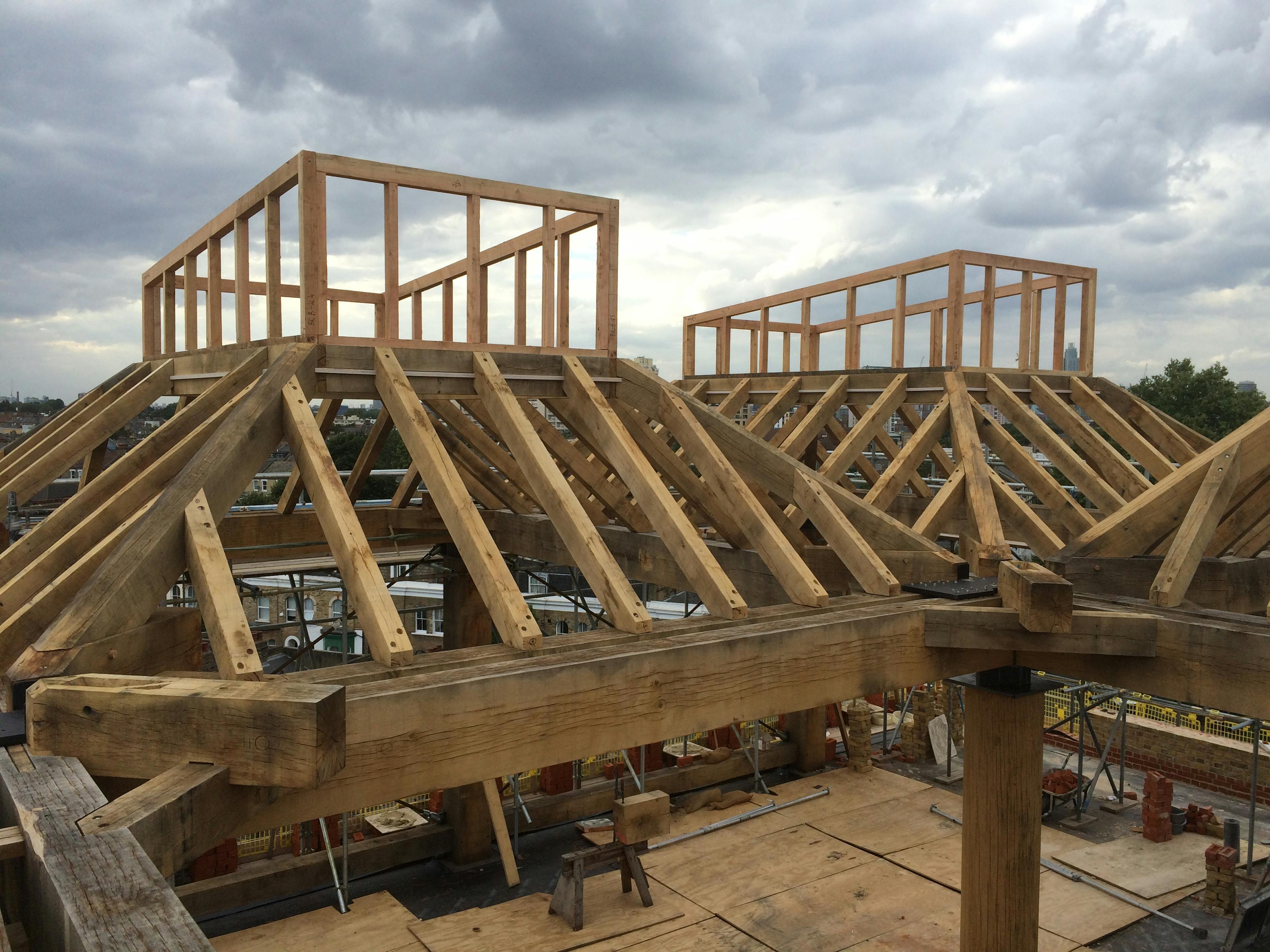 Oak lantern frames being constructed on a rooftop with cloudy skies behind