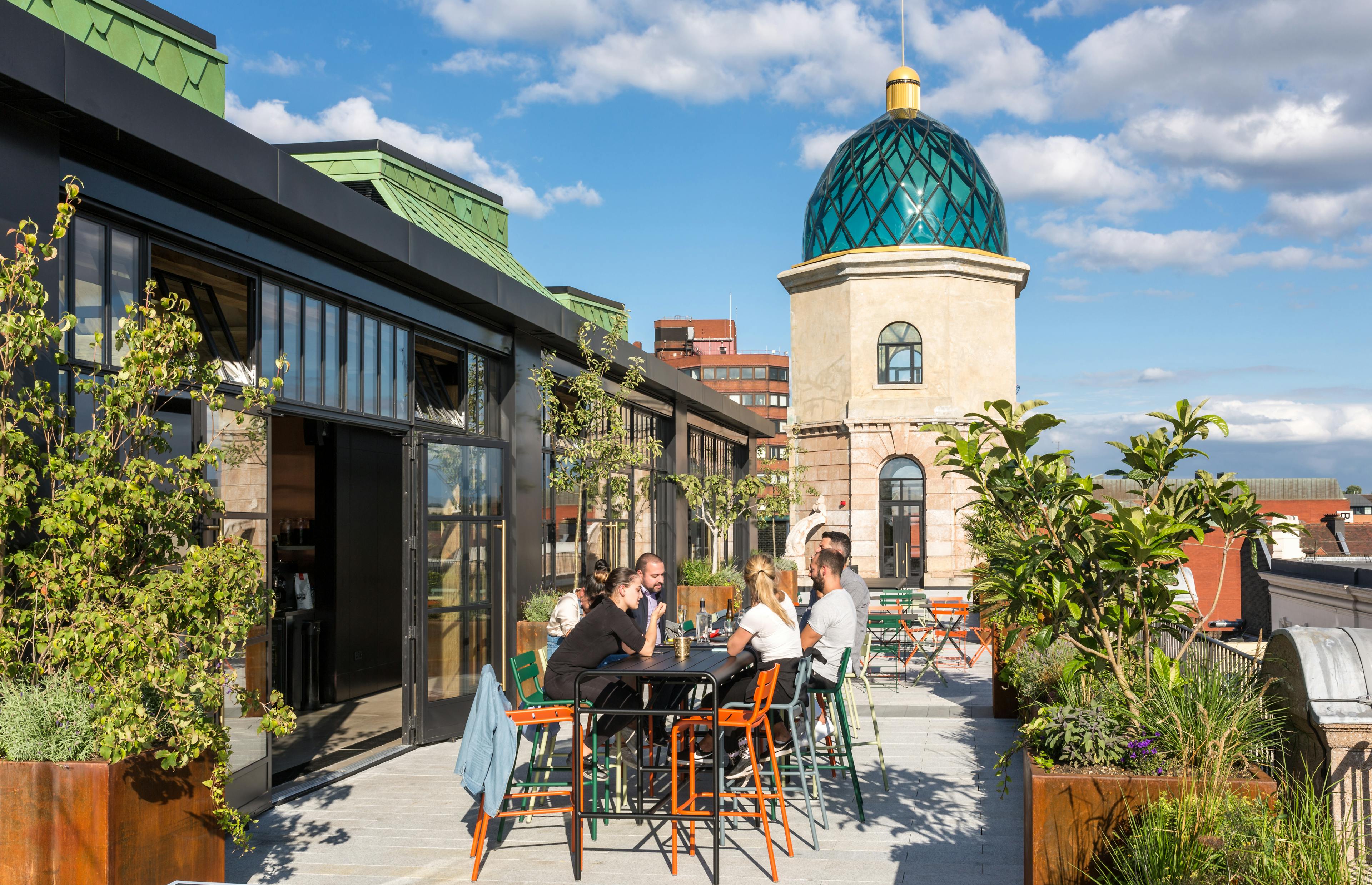 Customers sit at tables on a terrace outside a rooftop bar