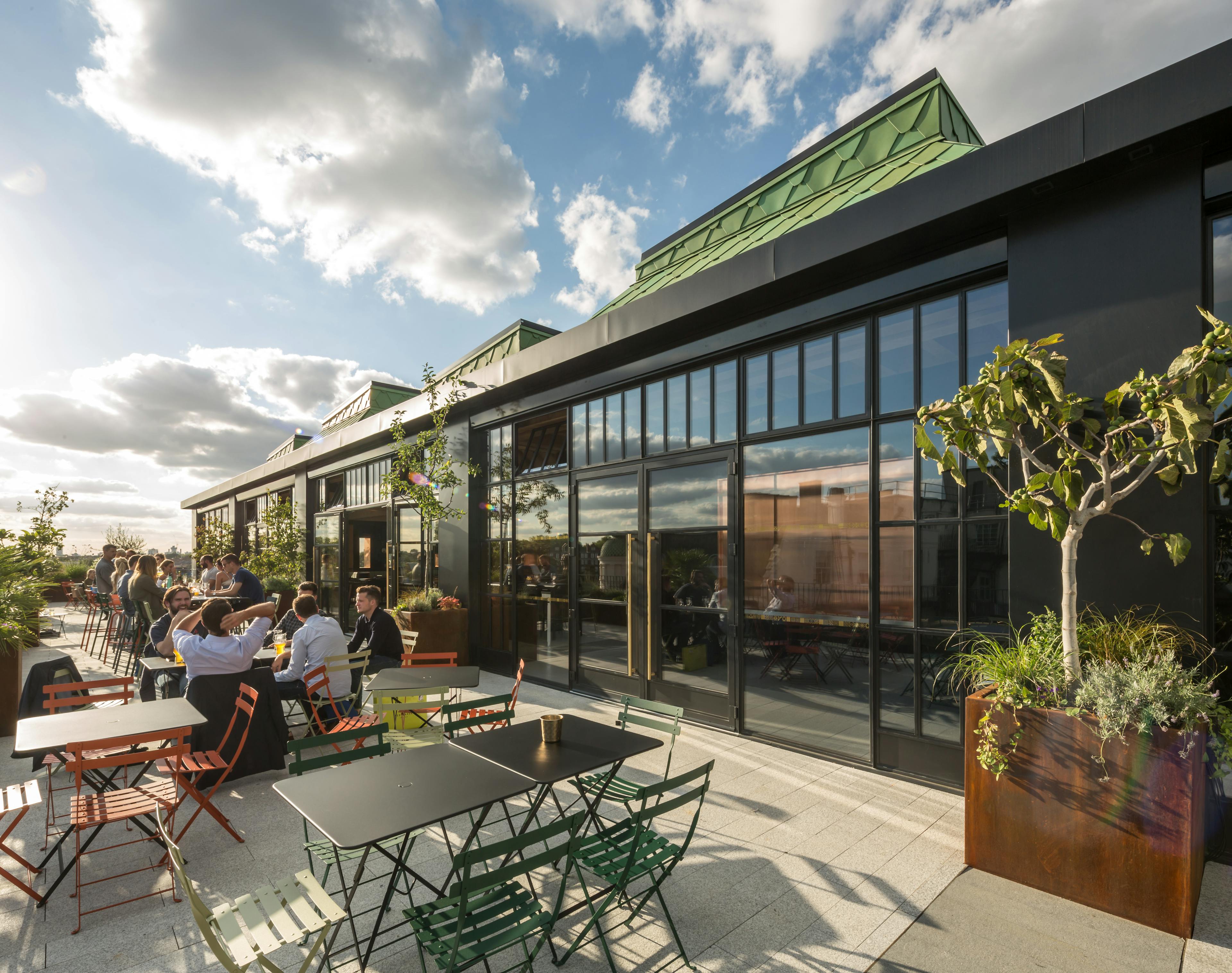 Customers sit at tables on a terrace outside a rooftop bar