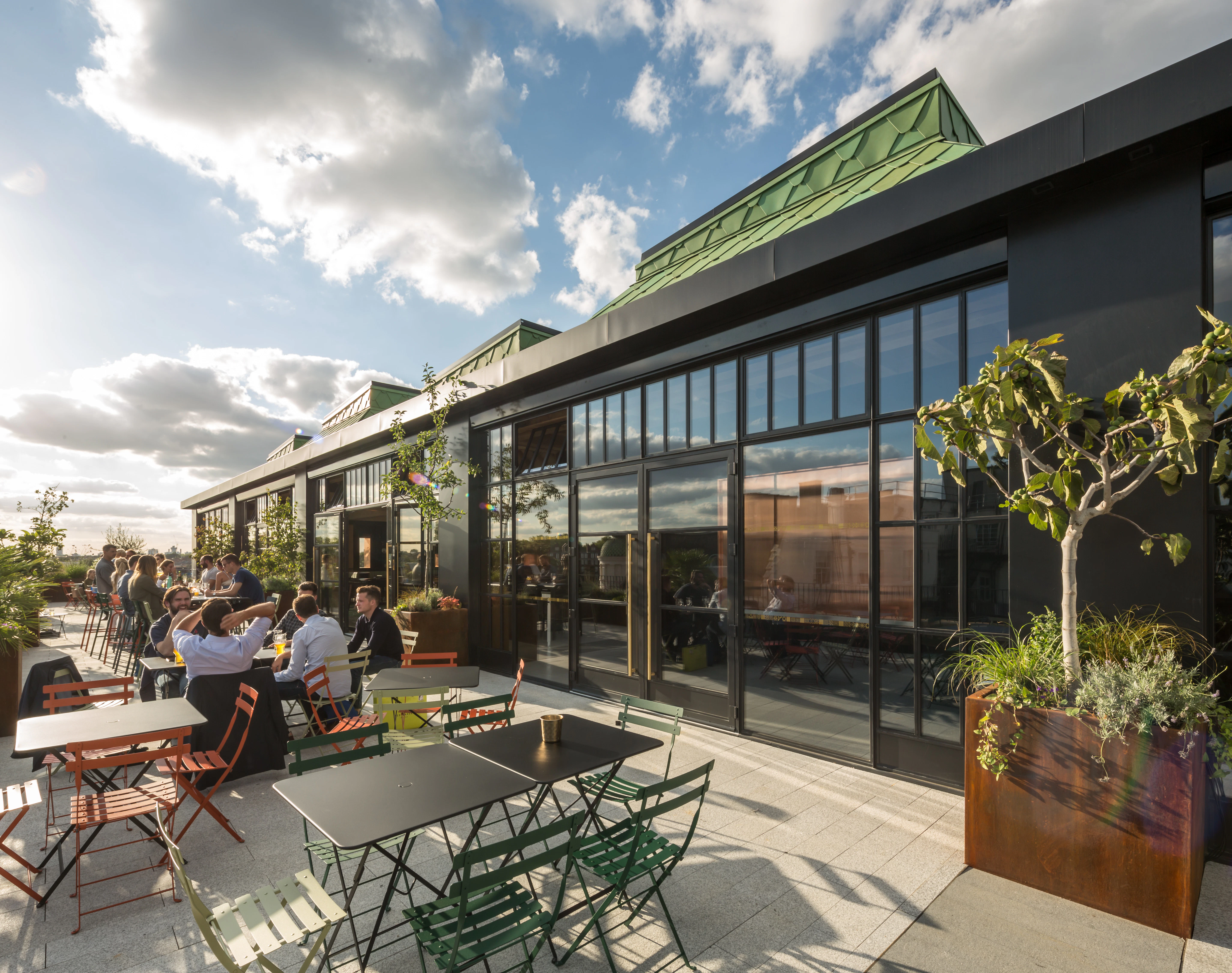 Customers sit at tables on a terrace outside a rooftop bar.