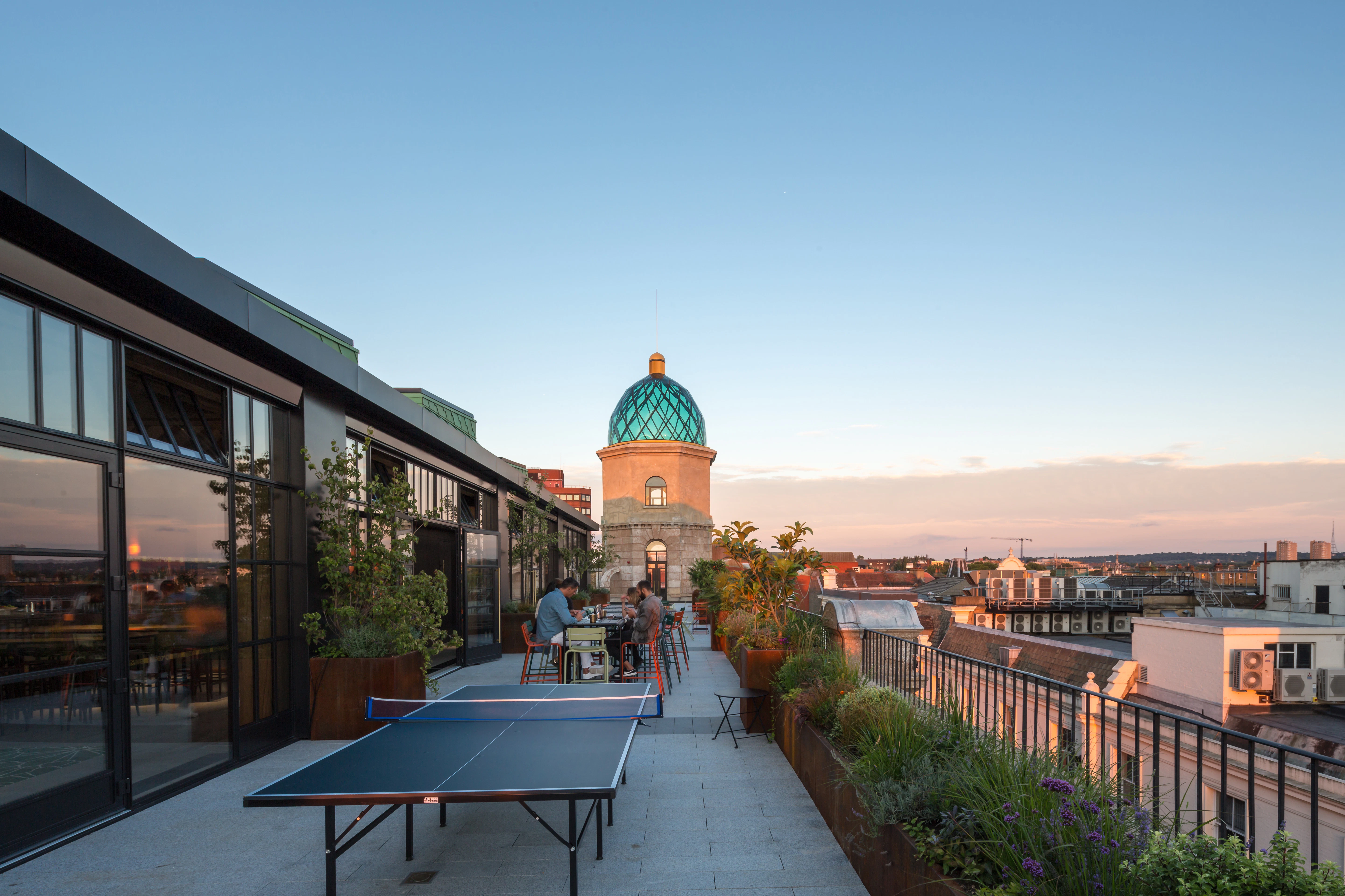 Customers sit at tables on a terrace outside a rooftop bar at dusk
