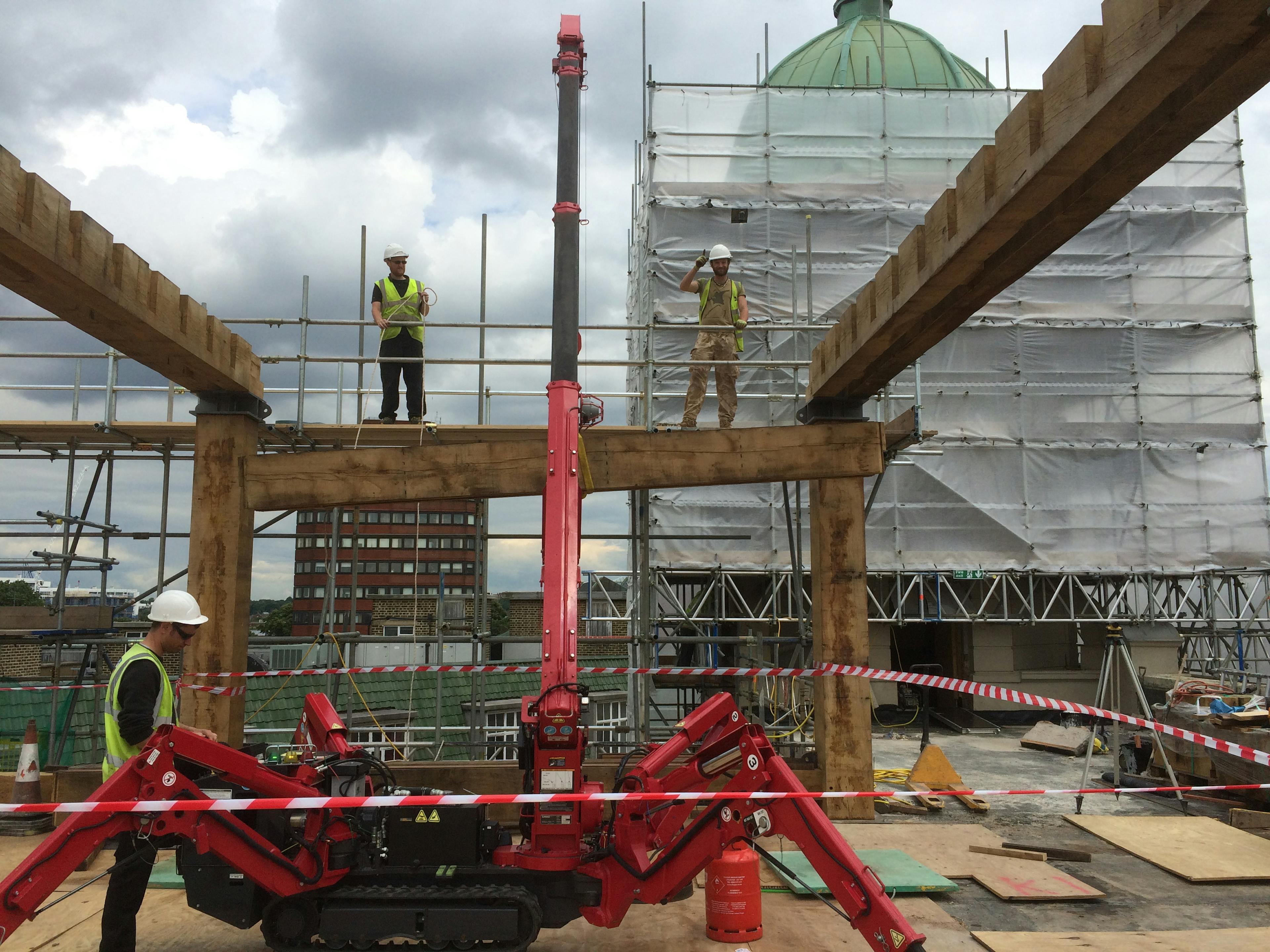Carpenters using  a red spider crane to put in place an oak frame on a rooftop in a city