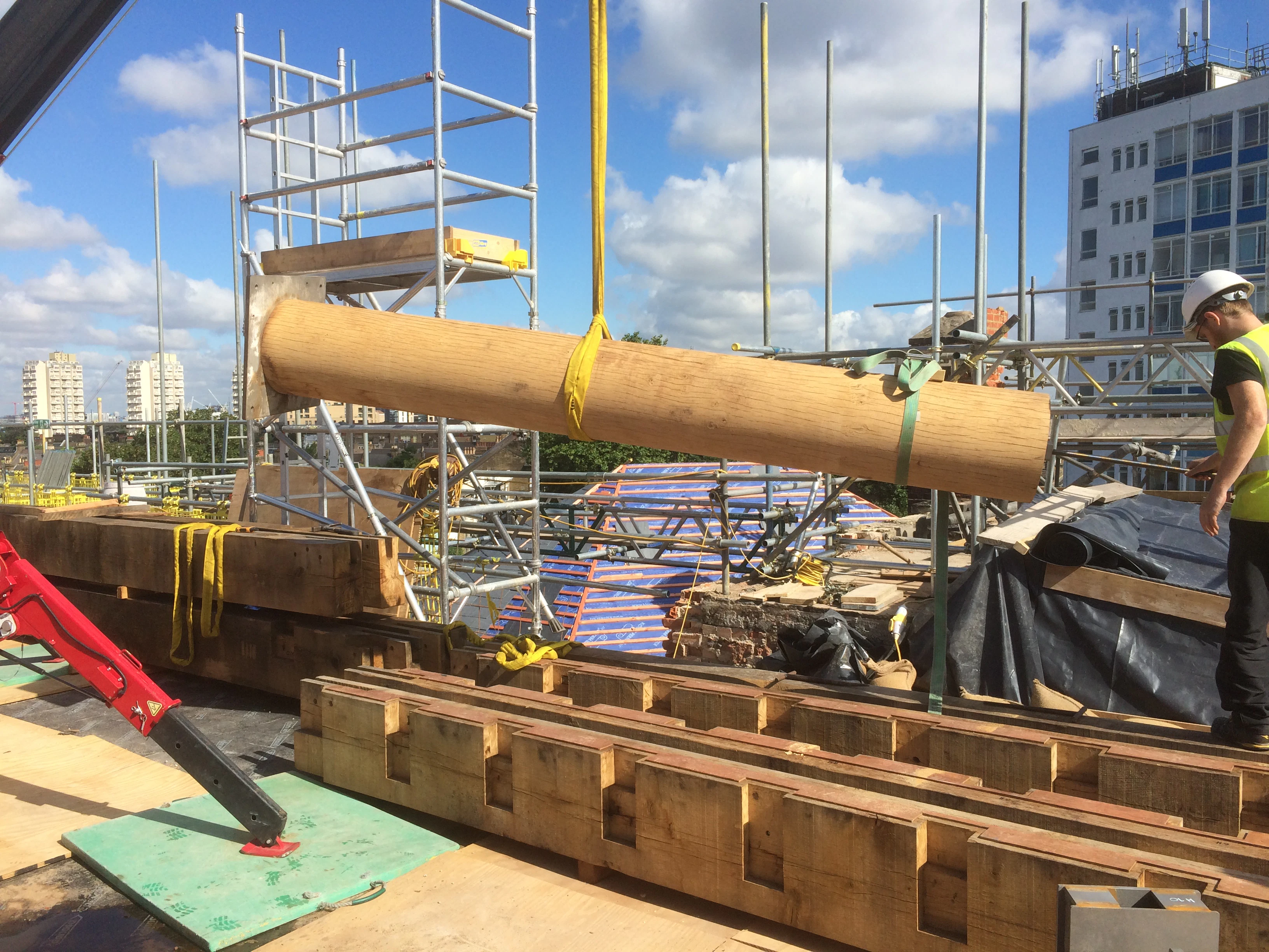 A round oak post held horizontally on tethers on a rooftop construction site