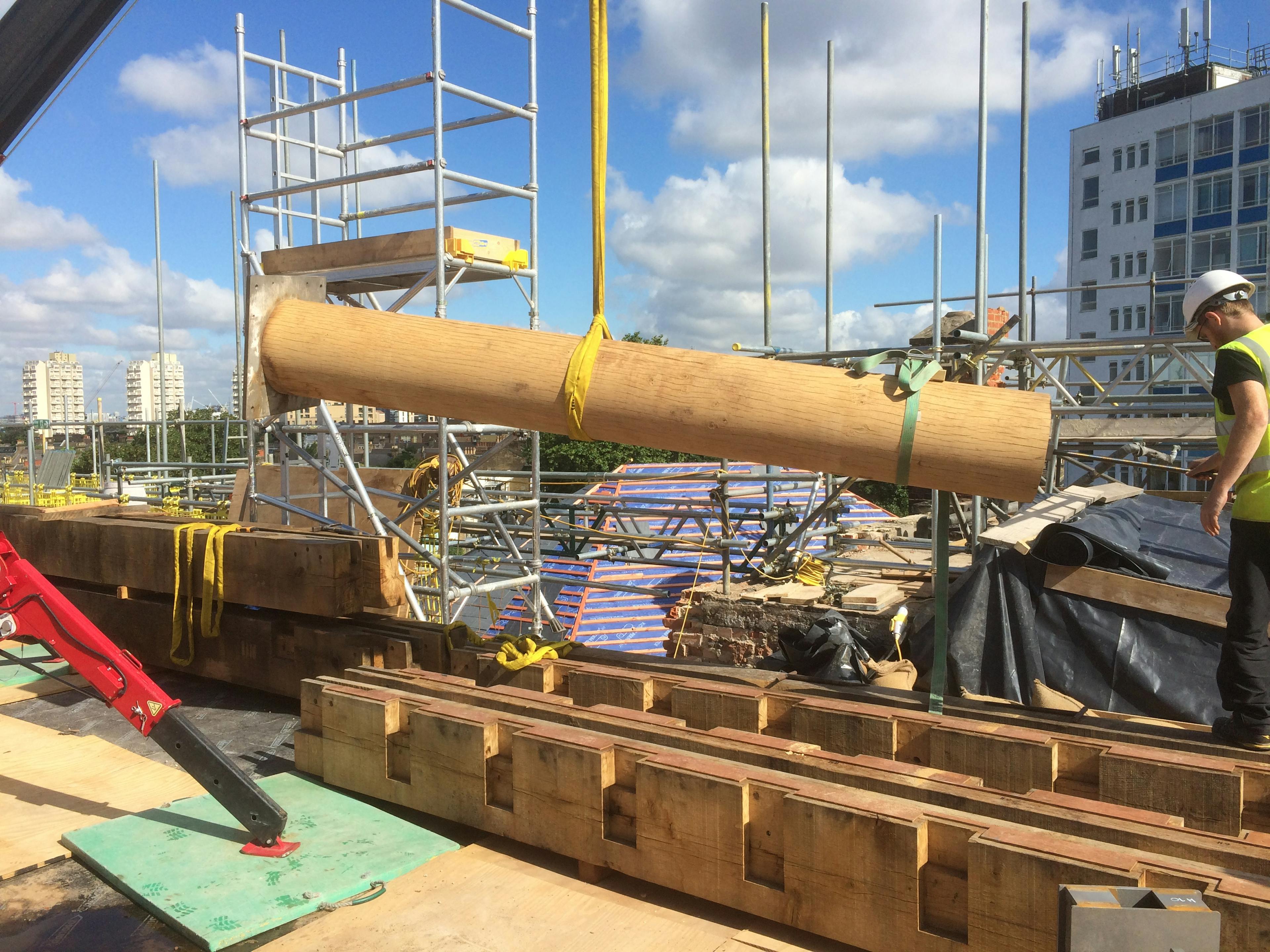 A round oak post held horizontally on tethers on a rooftop construction site