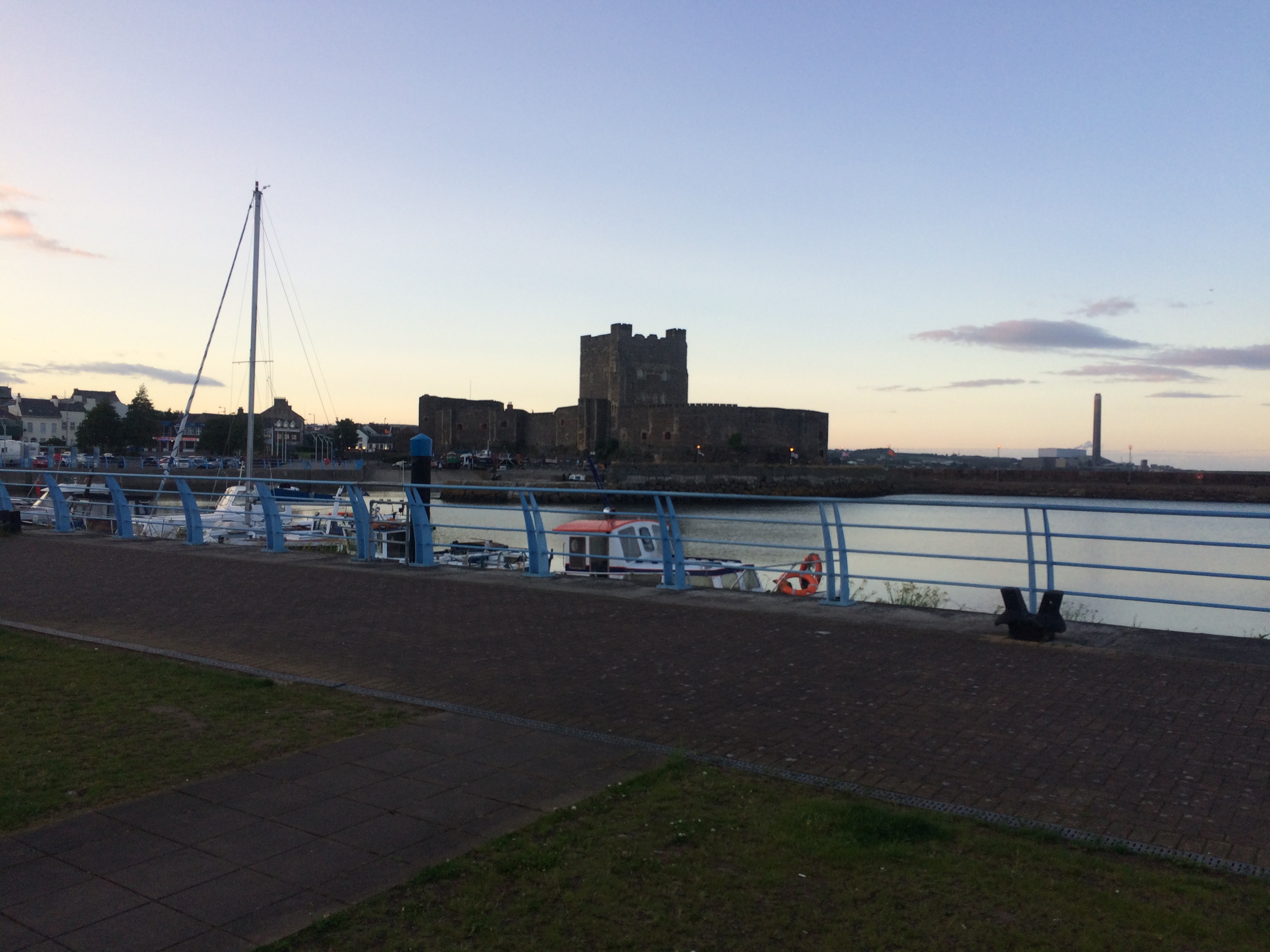 A 12th century stone castle with a large tower seen across a harbour is silhouetted at dusk 