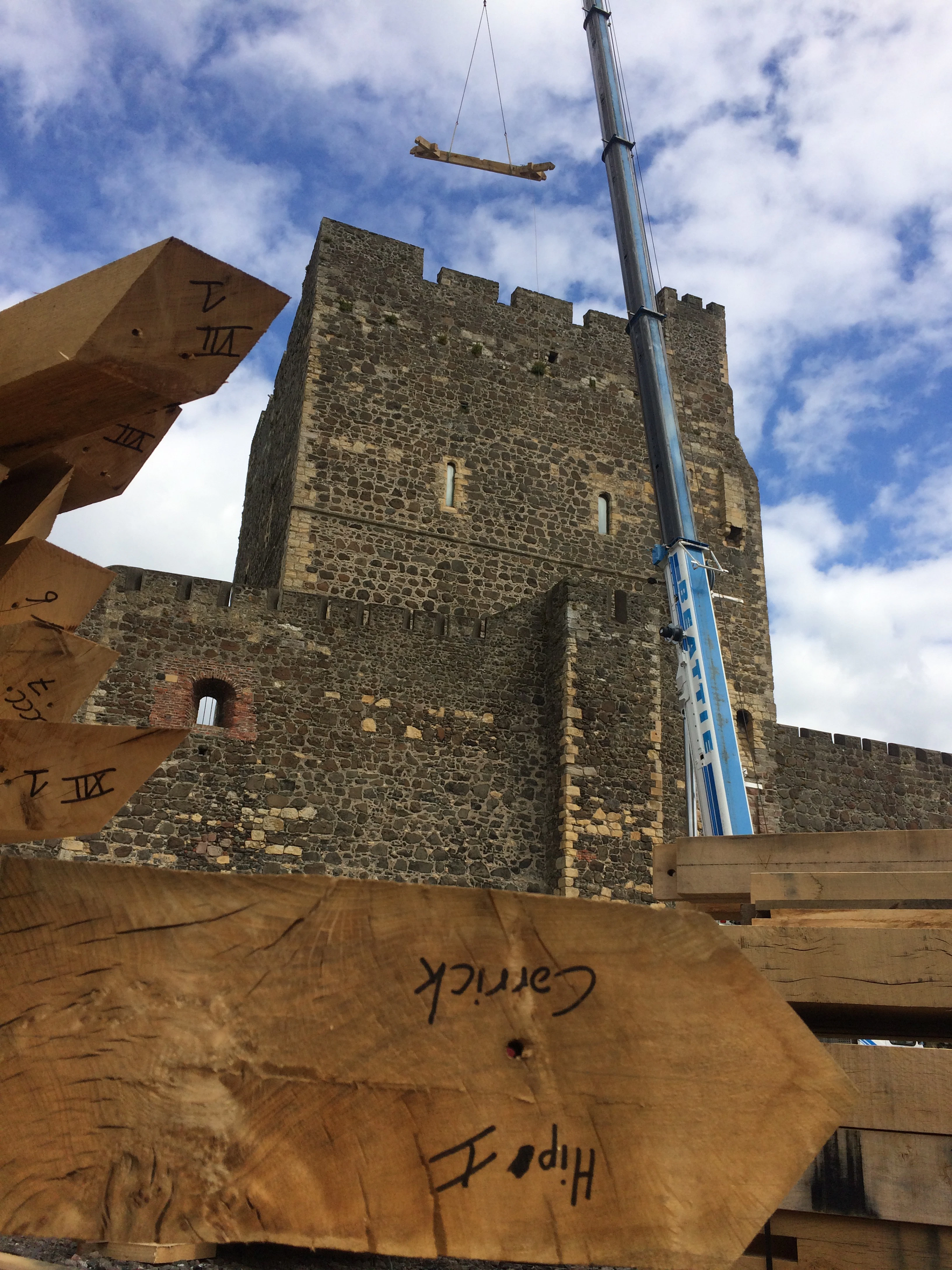 A piece of oak frame is lifted up by a crane onto a stone tower of a 12th century castle