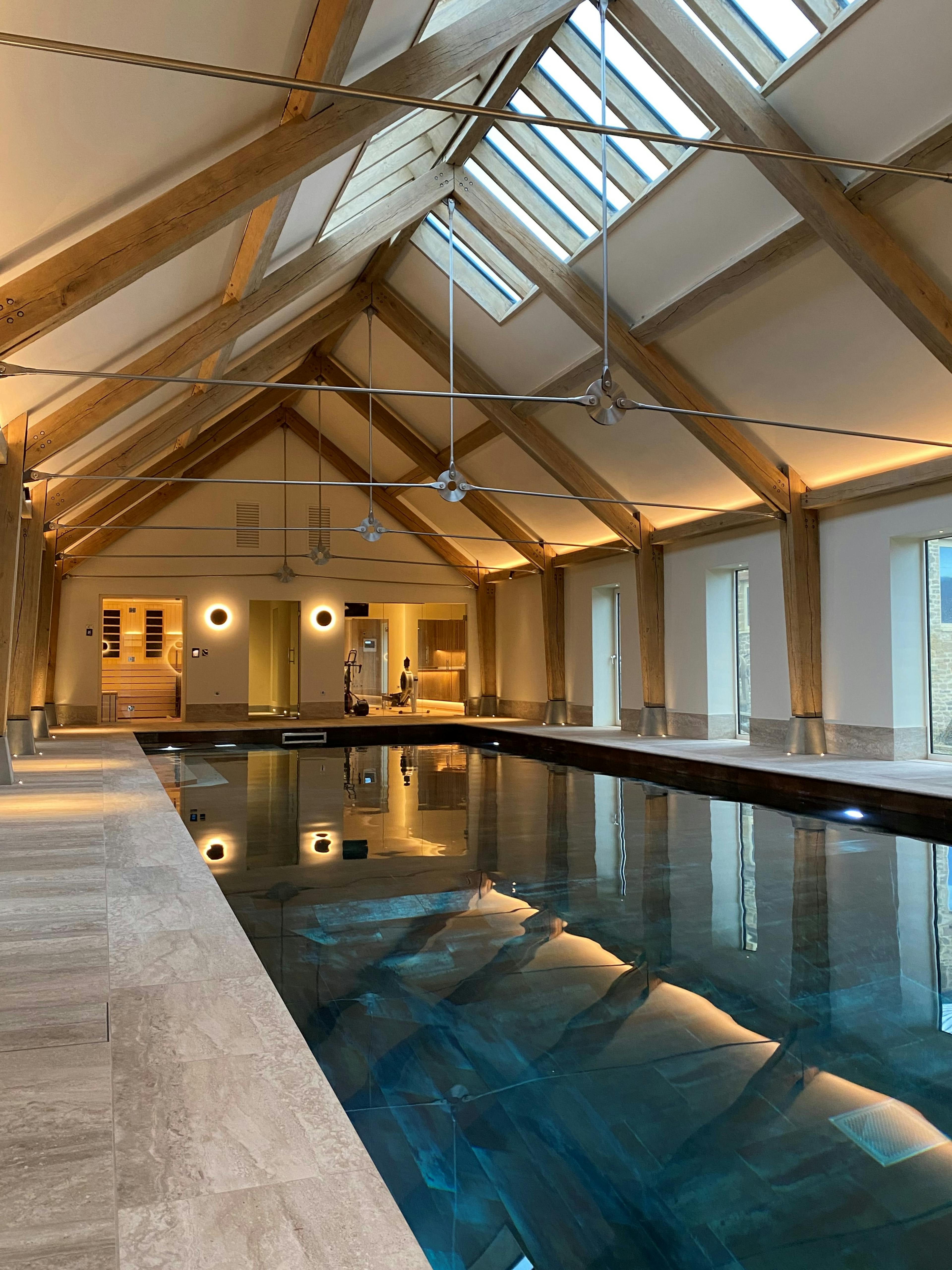 A swimming pool with an oak frame and steel tie connections, windows on the side and rooflights