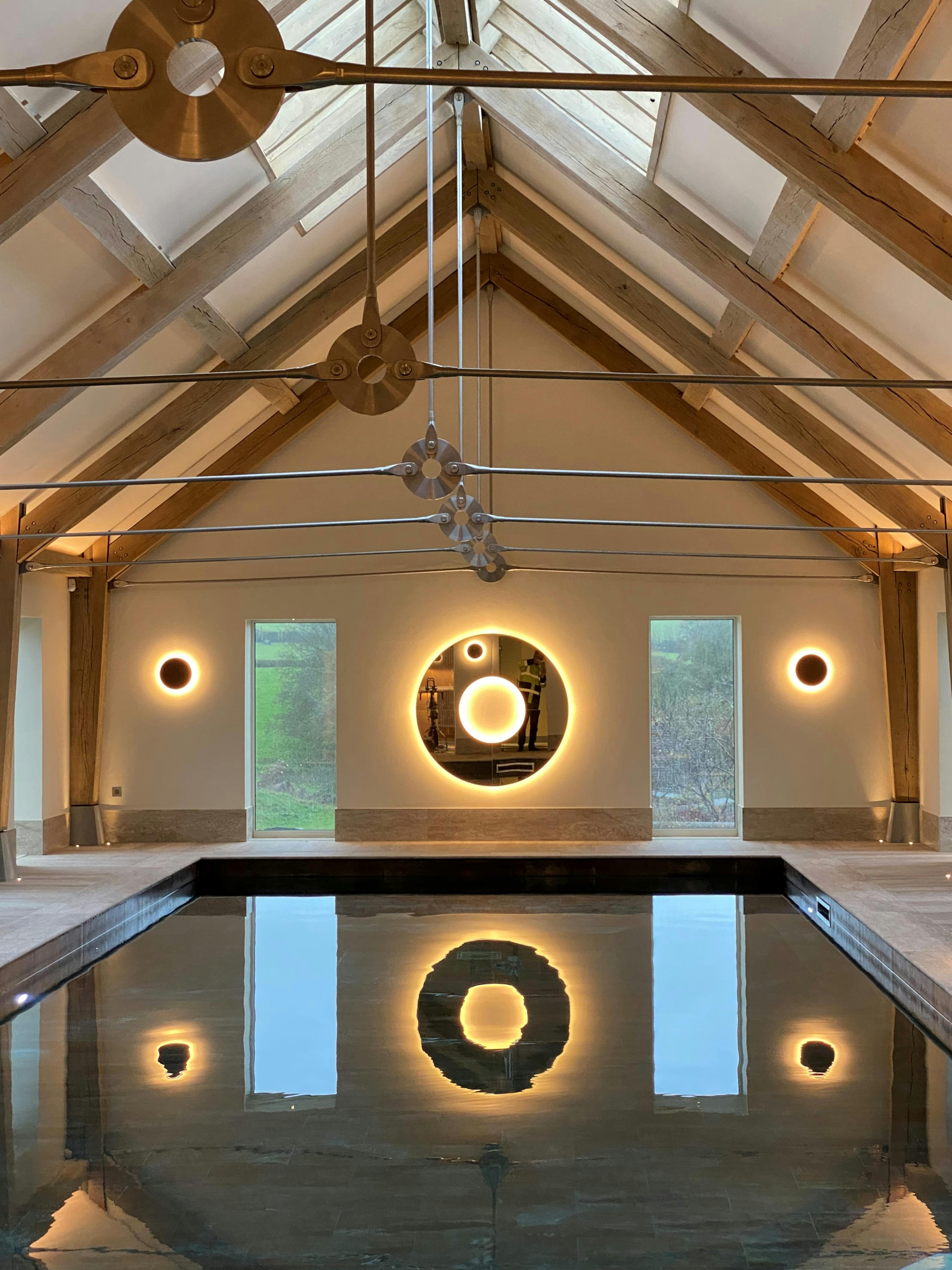 A swimming pool with an oak frame and steel tie connections, windows on the side and rooflights