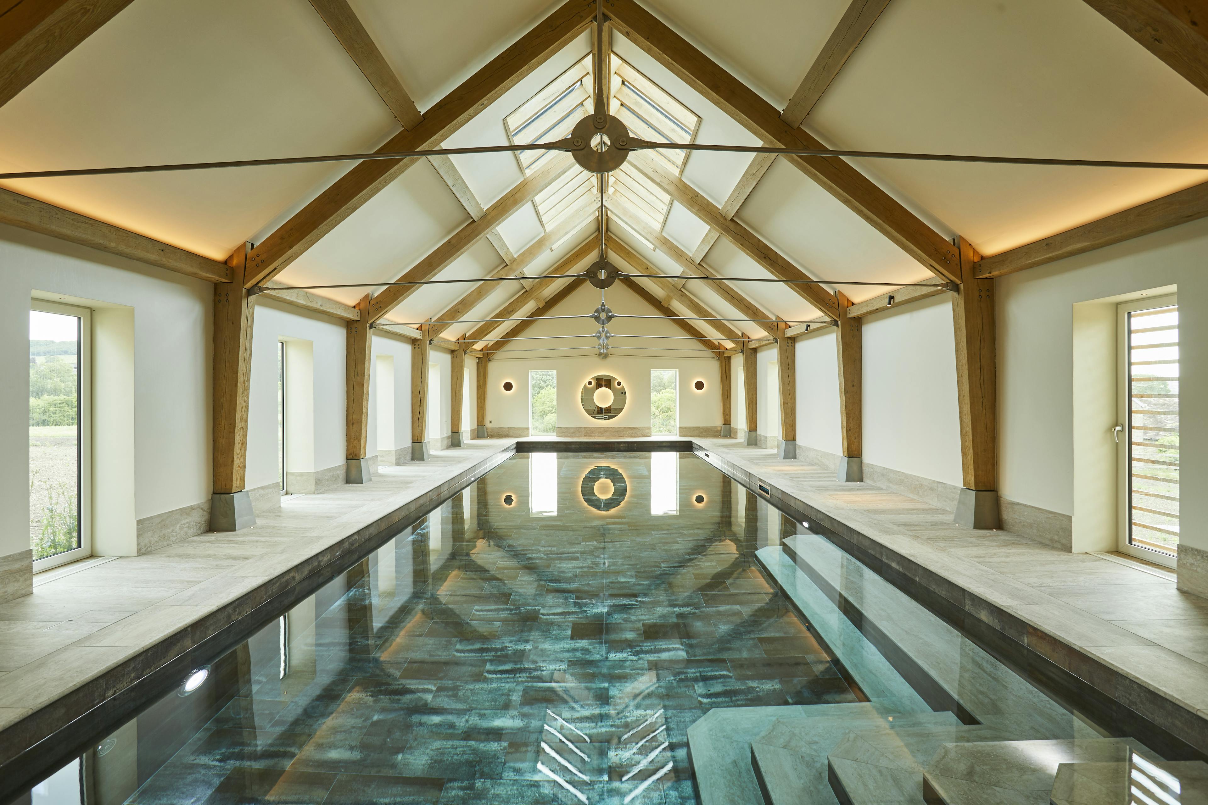 A swimming pool with an oak frame and steel tie connections, windows on the side and rooflights
