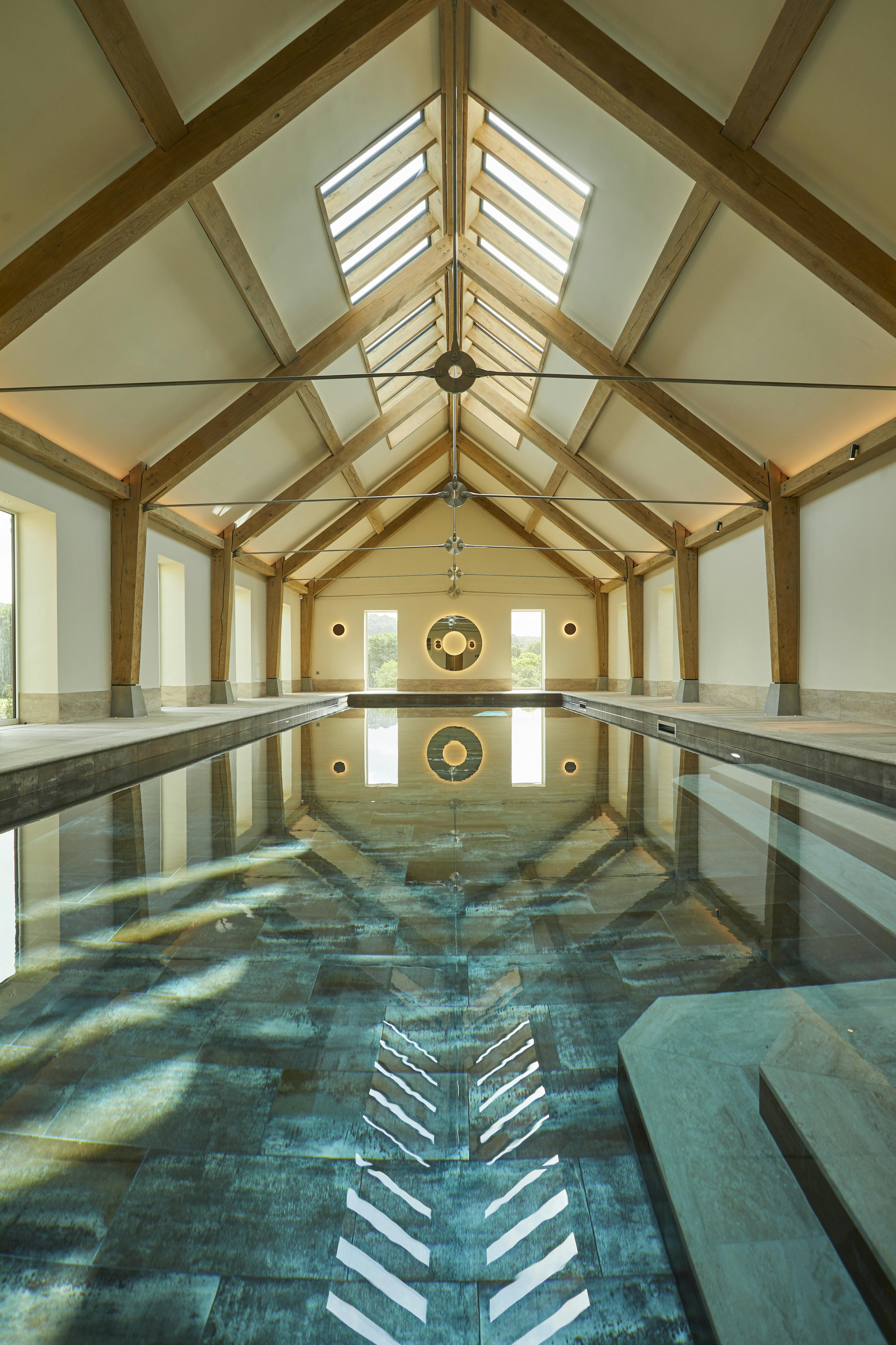 A swimming pool with an oak frame and steel tie connections, windows on the side and rooflights